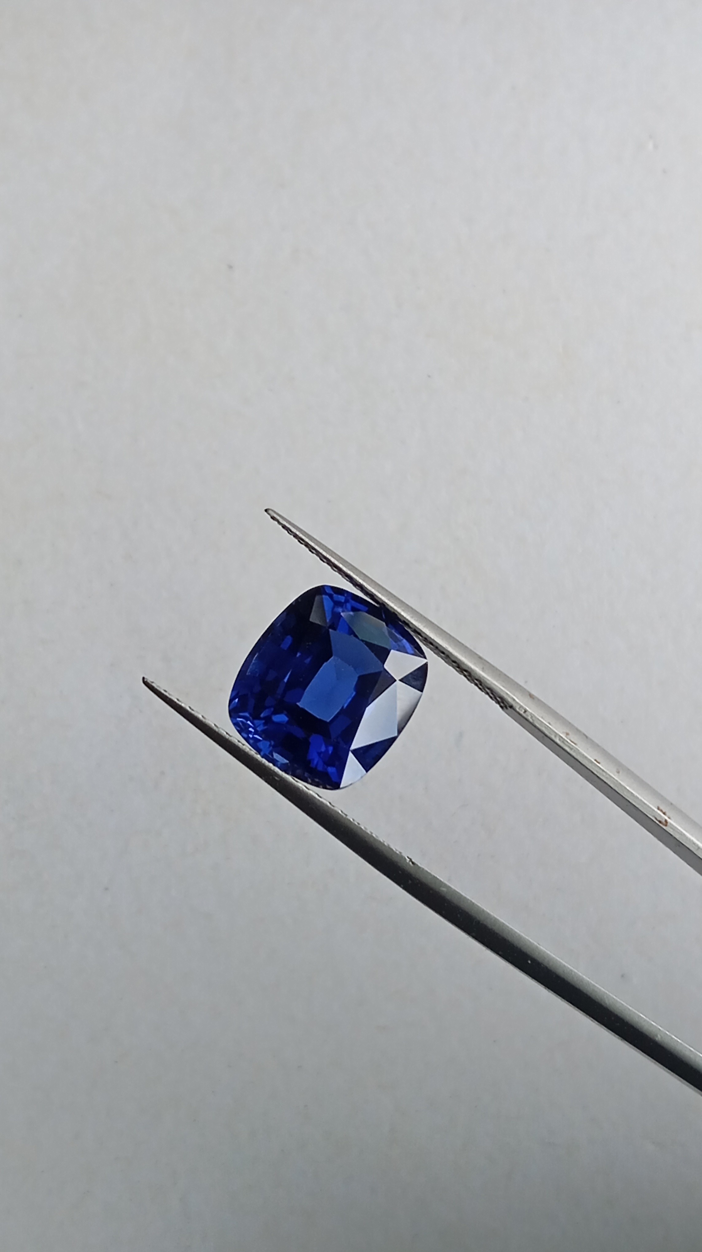 A vivid royal blue heart-shaped lab-grown sapphire gemstone held in tweezers for scale.
