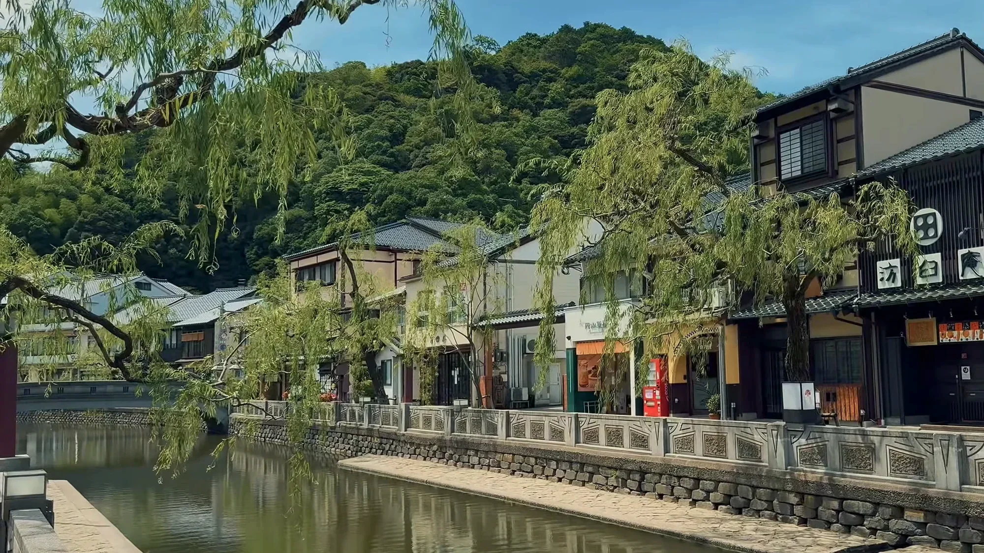 The canal at Kinosaki Onsen in summer, willows trailing over the water and wooden inns along the stone embankment.