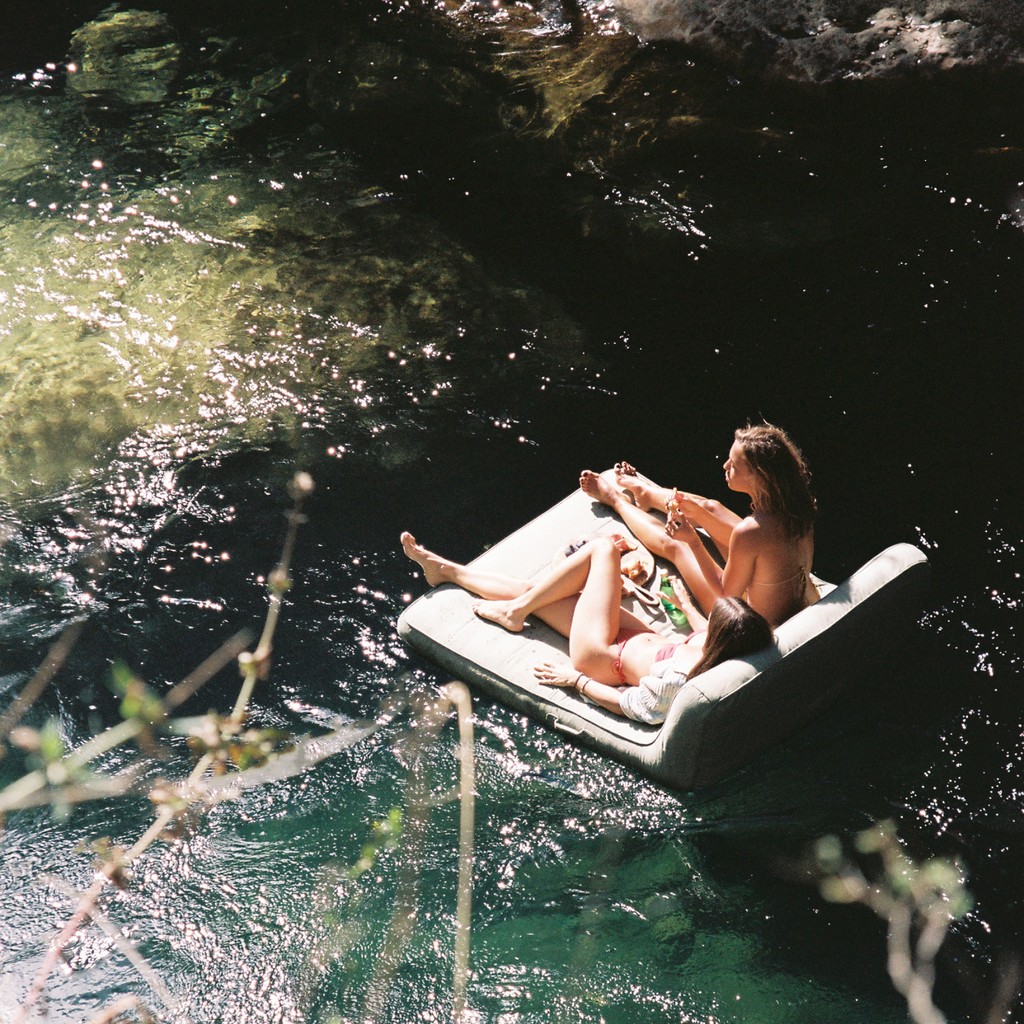 Woman floating on a luxury green pool float in a natural rock pool surrounded by sunlit cliffs
