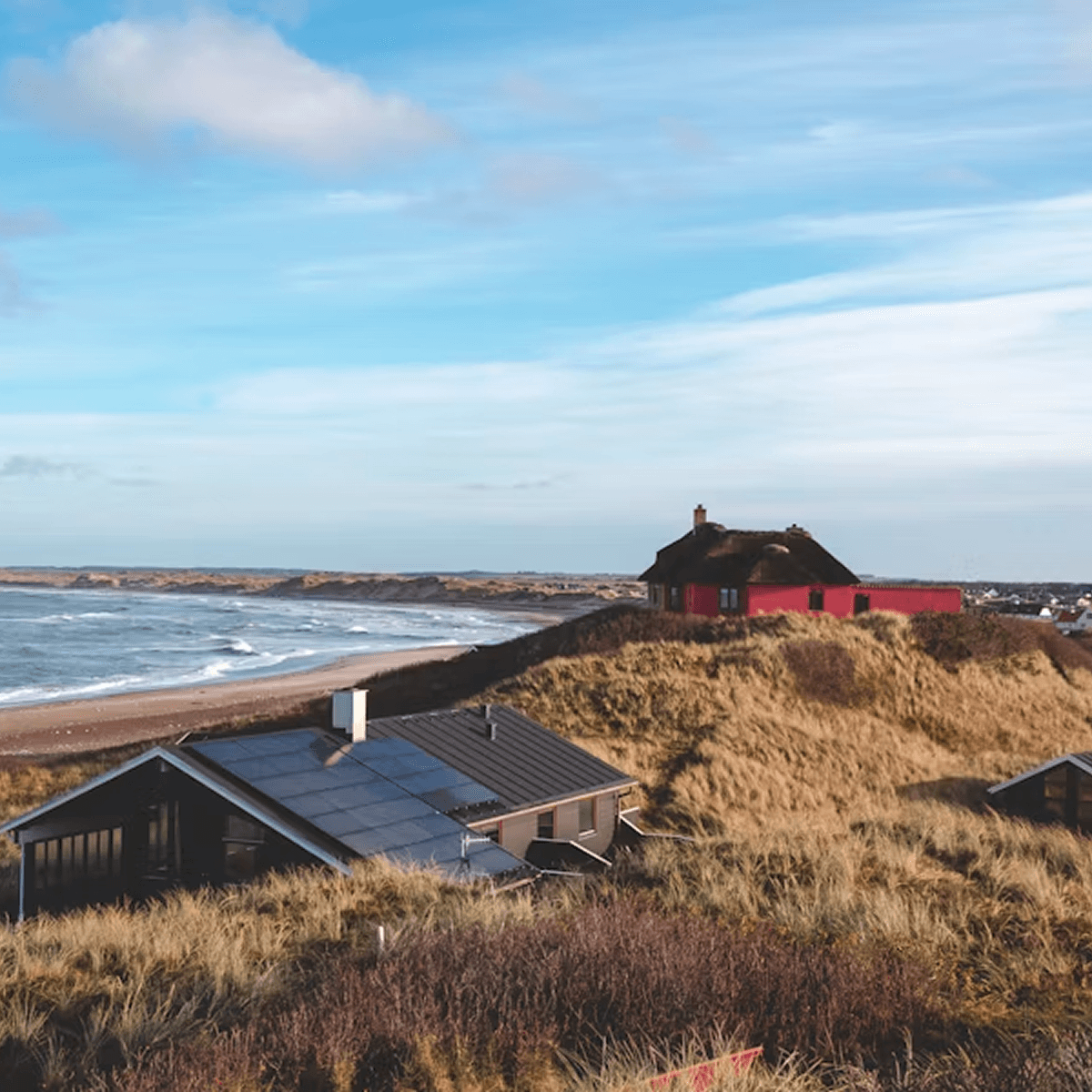 Coastal farmhouses on a windswept dune landscape under a cloudy sky, Denmark
