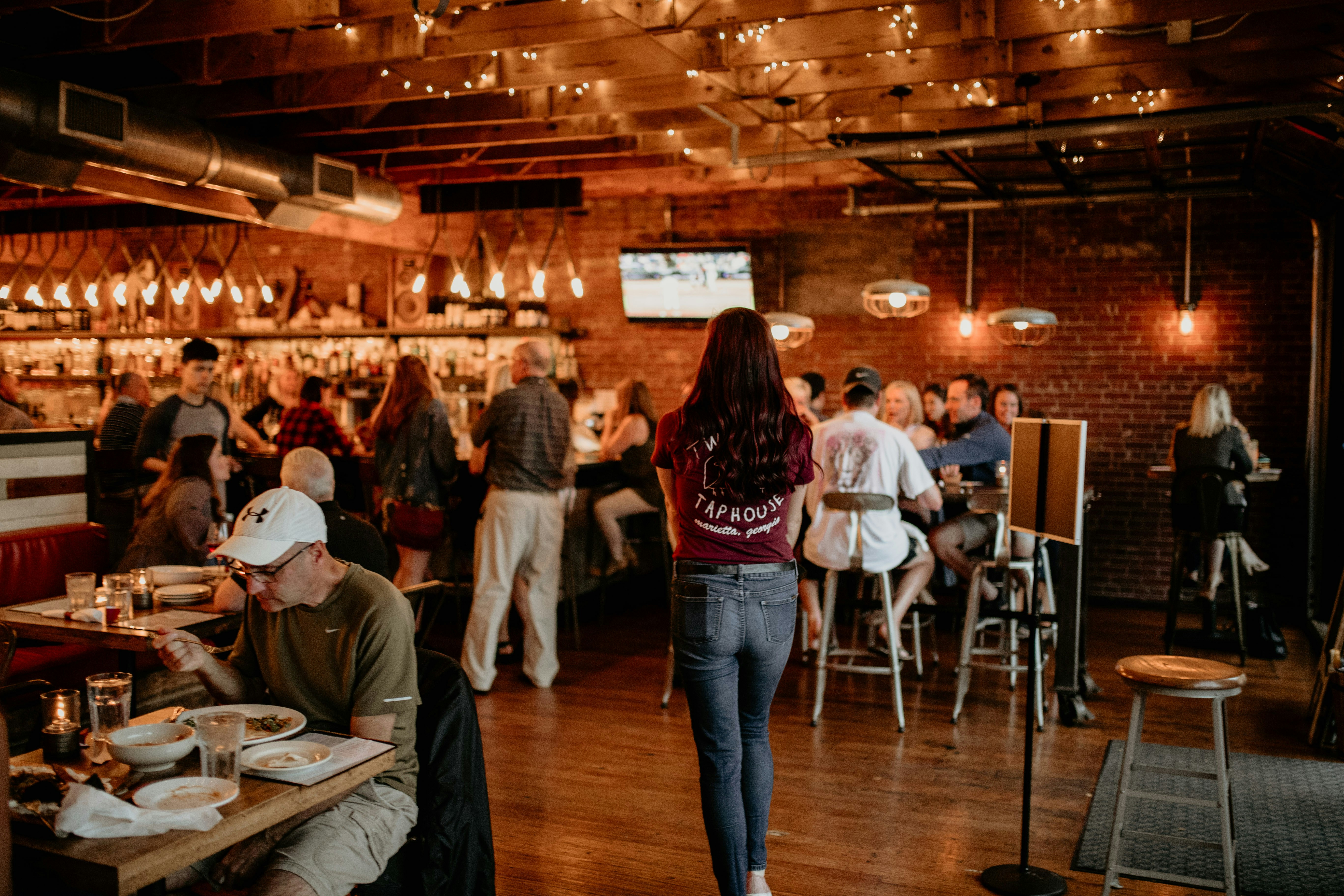 A busy taproom with wooden floors, tables and warm hanging lights