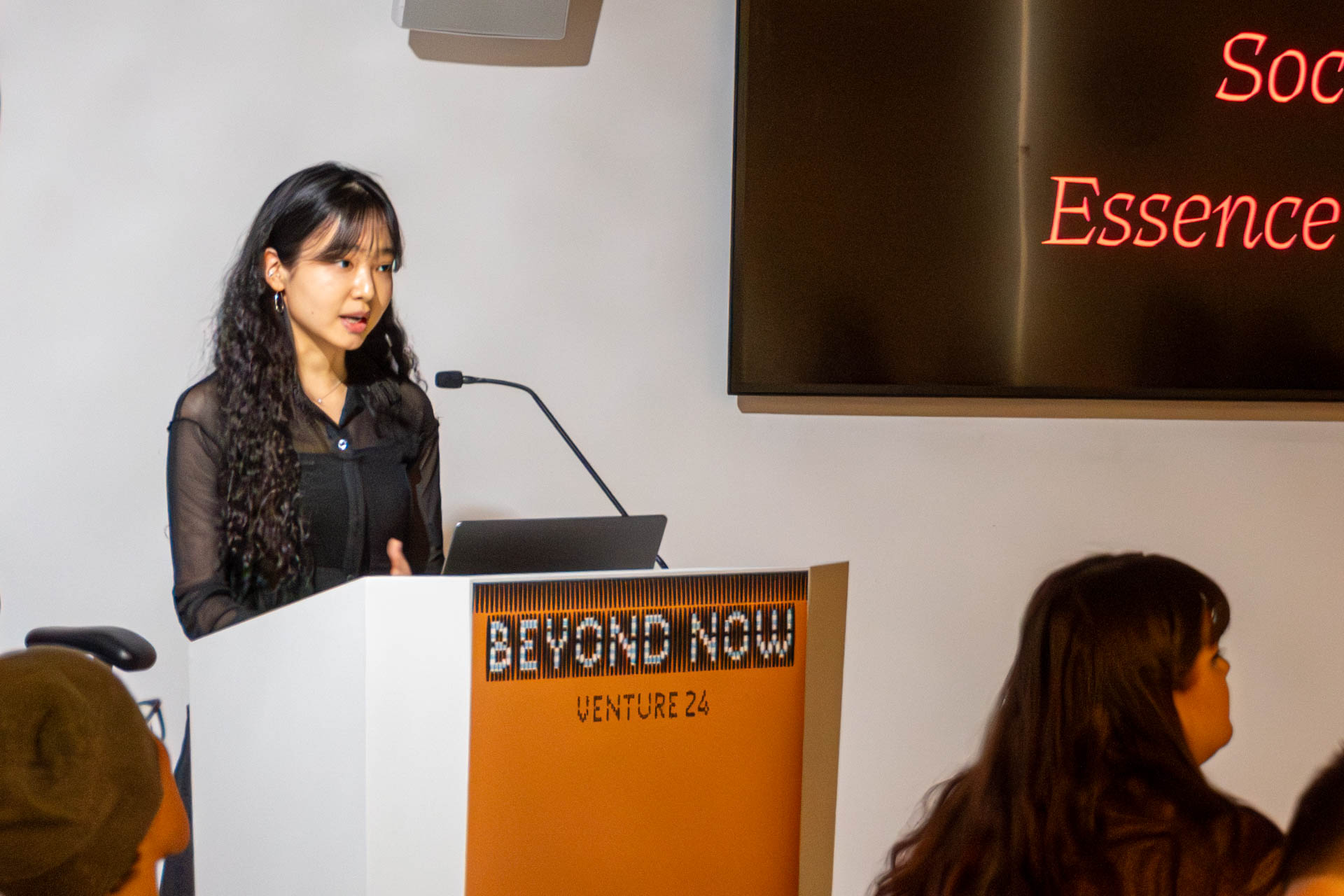A lady at the podium giving a presentation to a class.