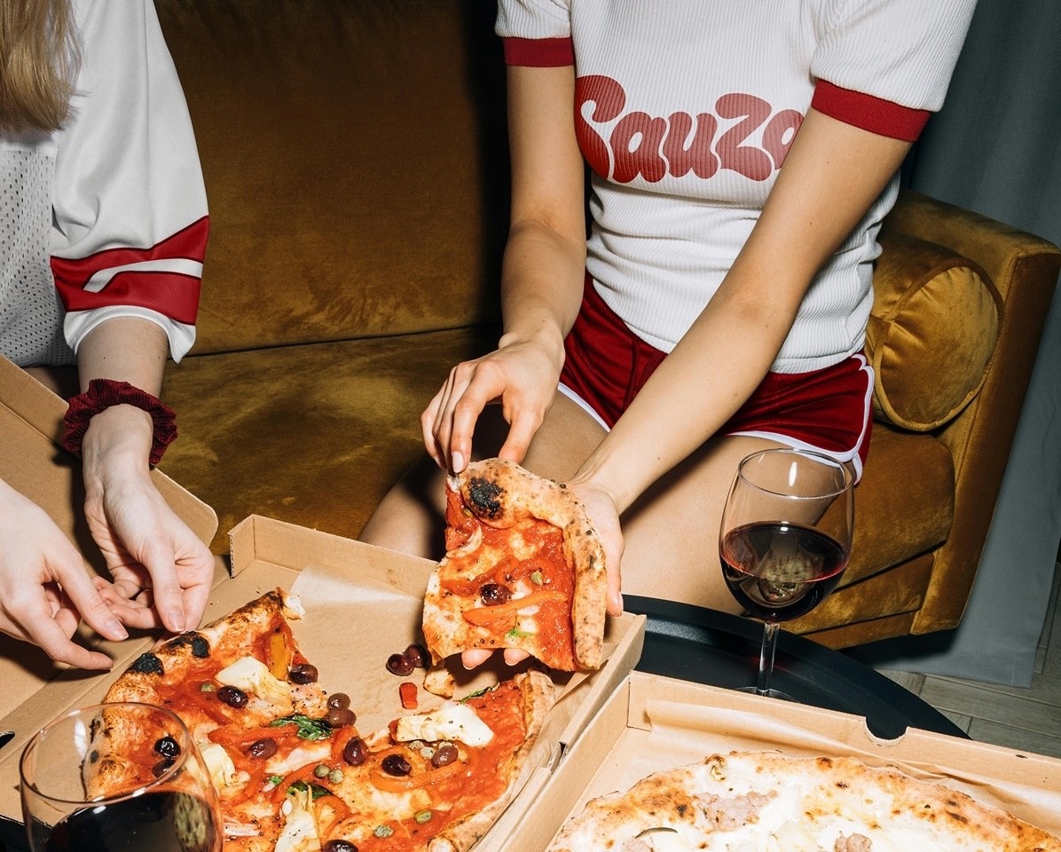 Friends sharing pizza and wine in a Sauza Pizzeria brand photography campaign.