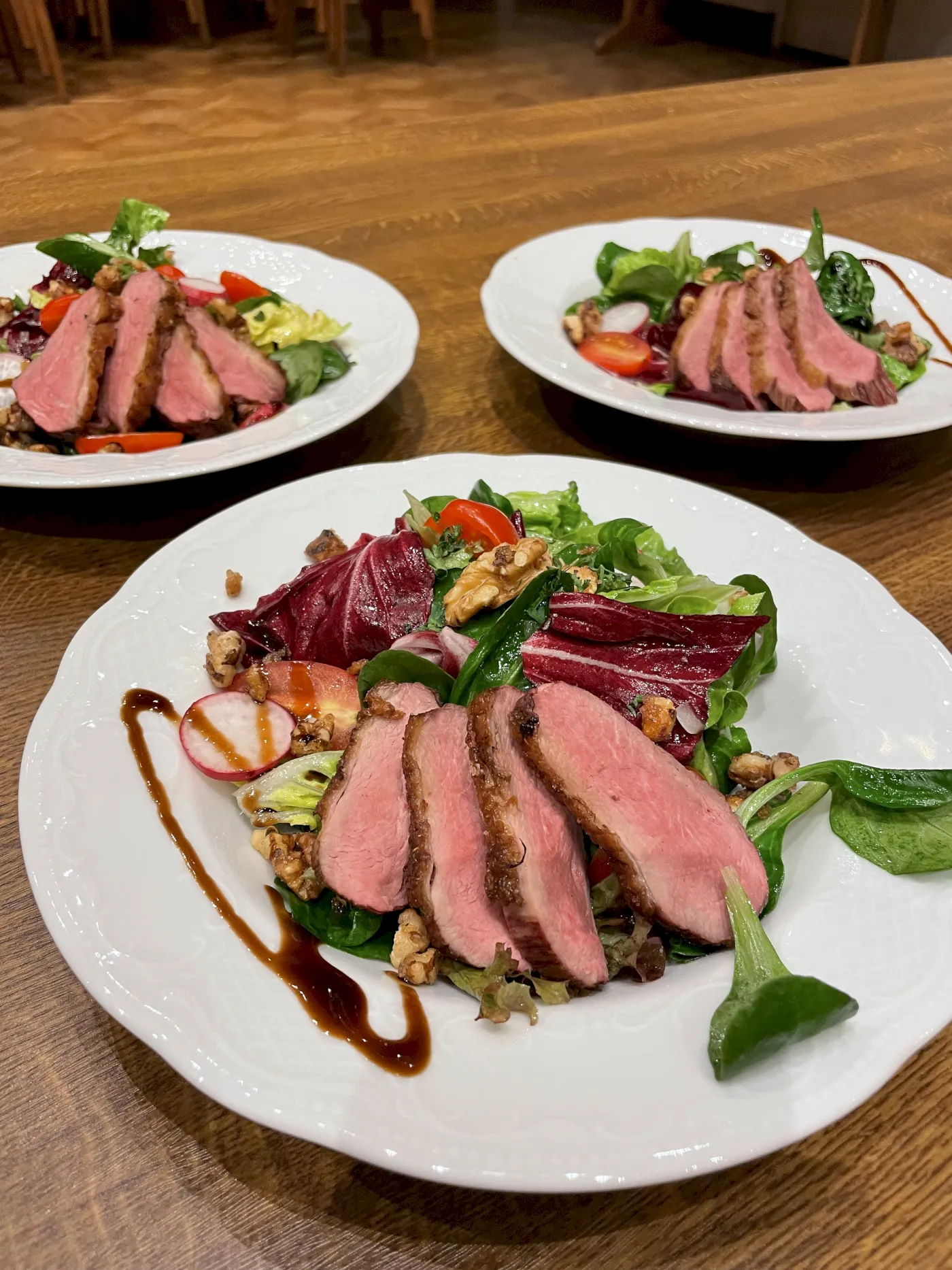 Drei Salatteller mit gebratenem Entenbrustfilet, Nüssen und frischem Gemüse auf einem Tisch.