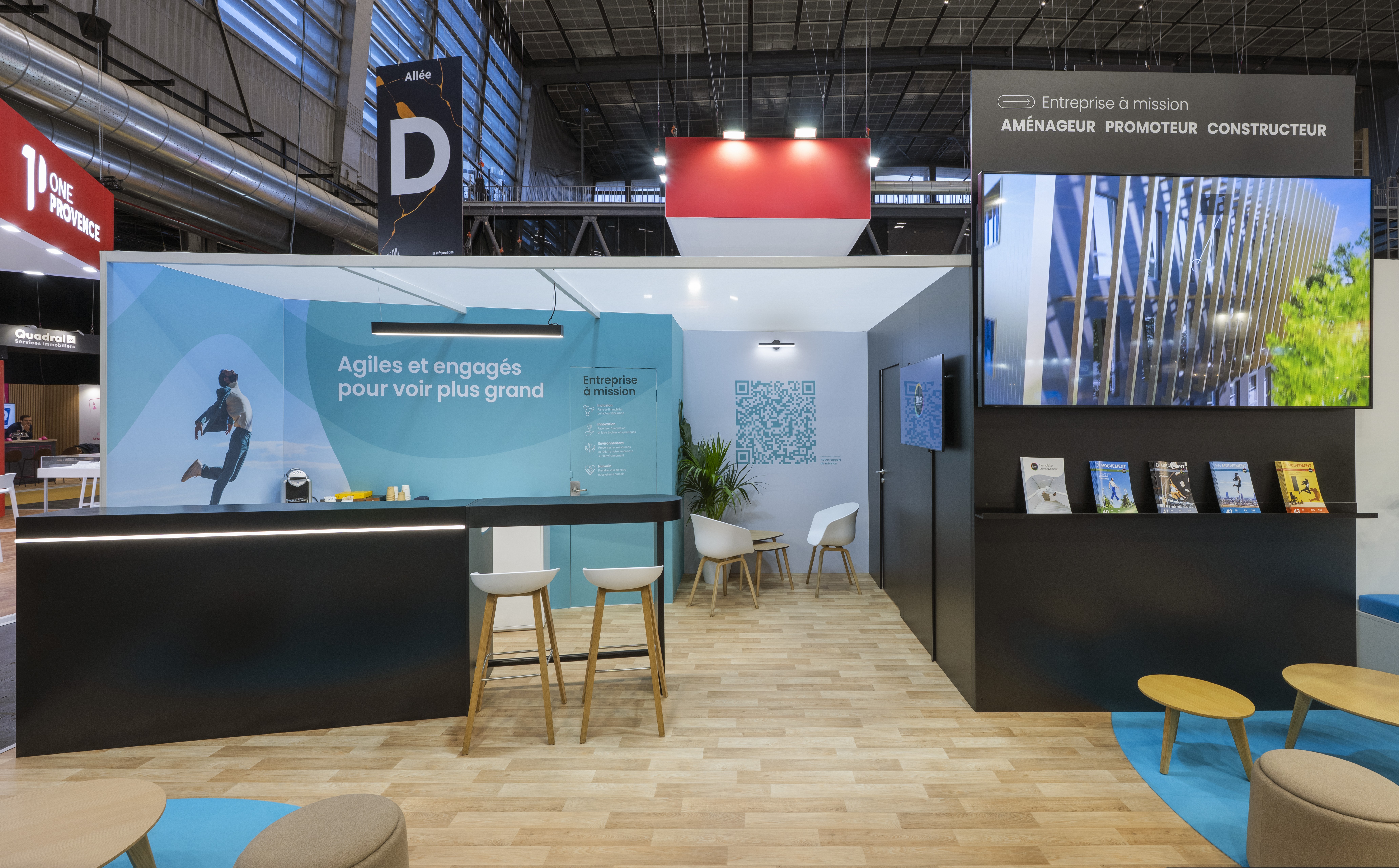 Stand EM2C SIMI 2025 Paris par Expace – vue intérieure avec espace lounge mobilier contemporain, sol clair, identité turquoise et noire et signalétique l'immobilier en mouvement