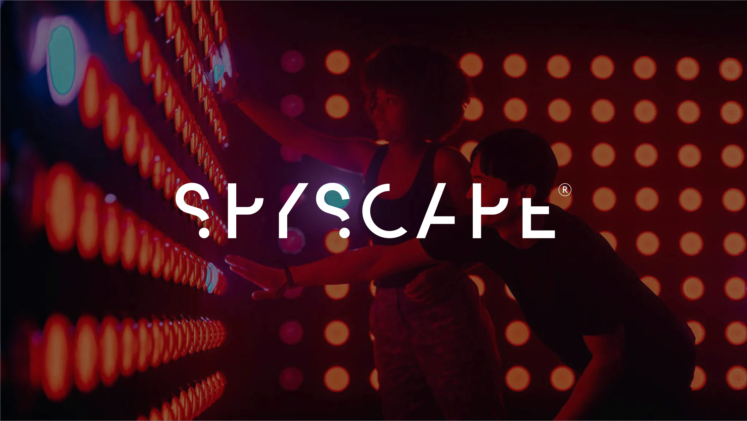 Person interacting with blue illuminated wall inside SPYSCAPE, with the SPYSCAPE logo overlaid.