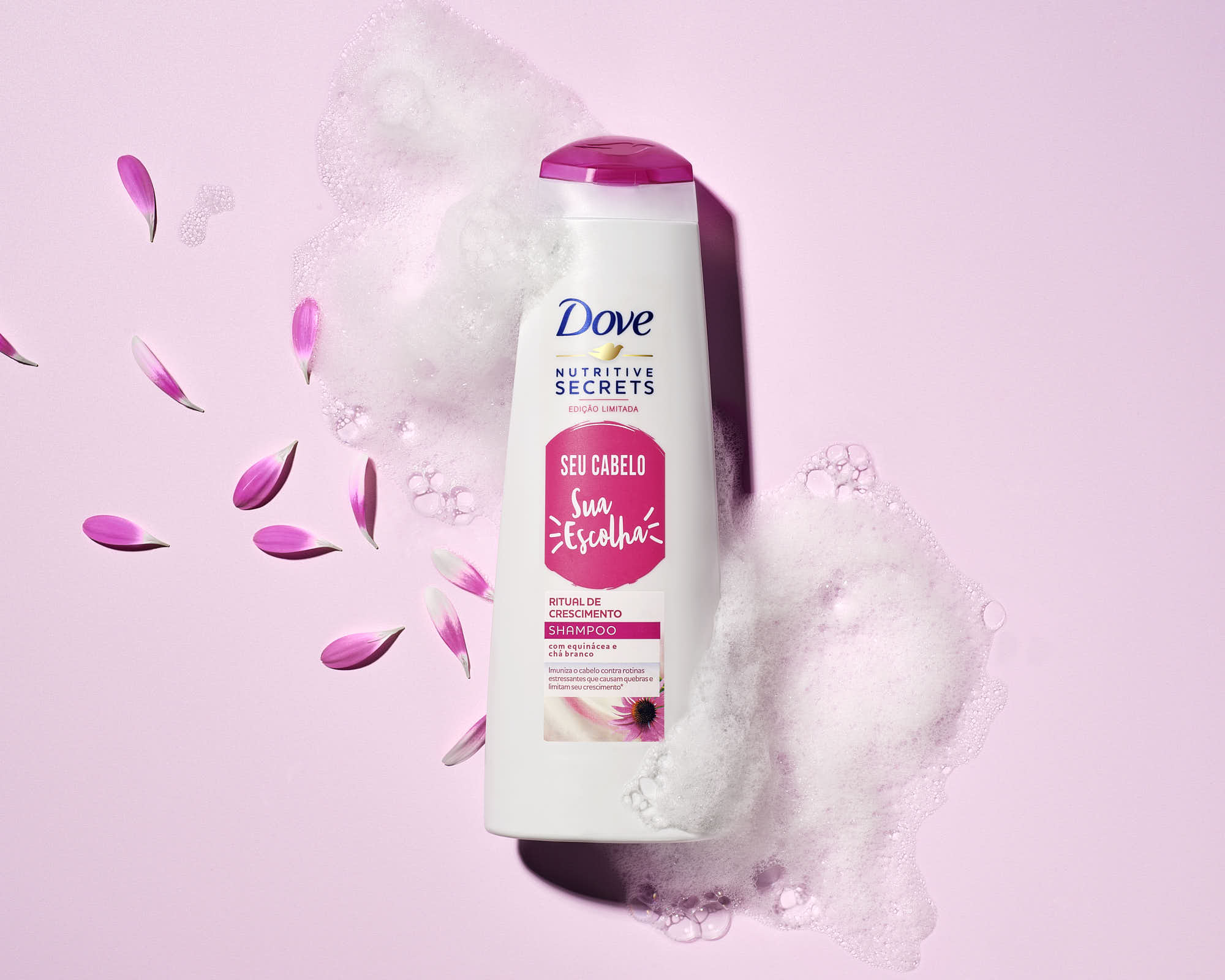 A bottle of hair conditioner on a pink background, surrounded by flower petals and cotton.