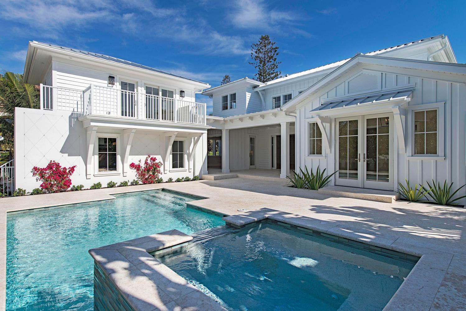 a luxurious pool surrounded by white tile and a classic, large white home