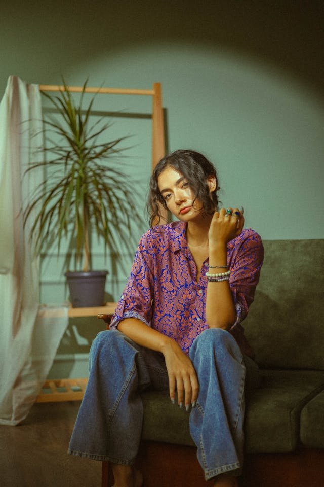 A woman in a colorful patterned shirt and jeans sits on a couch