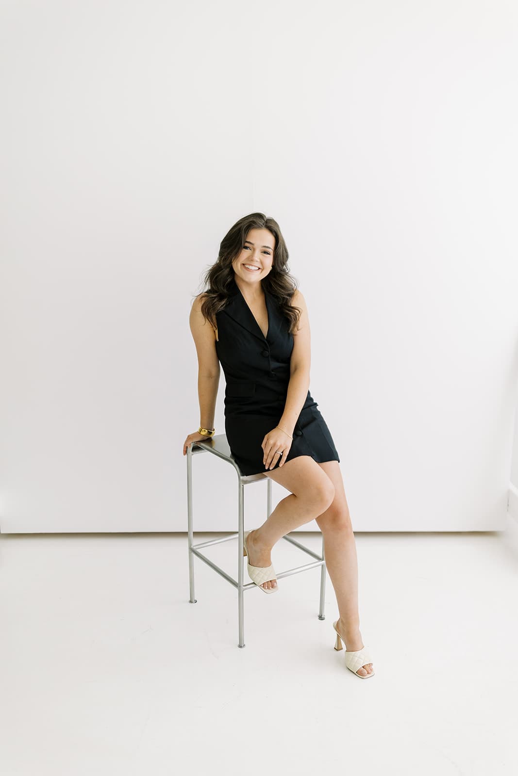 A model in a black dress sits confidently on a stool at Revelator Studio in Shreveport, photographed by Andy Roberts, showcasing the studio’s bright, minimalist space perfect for professional shoots.