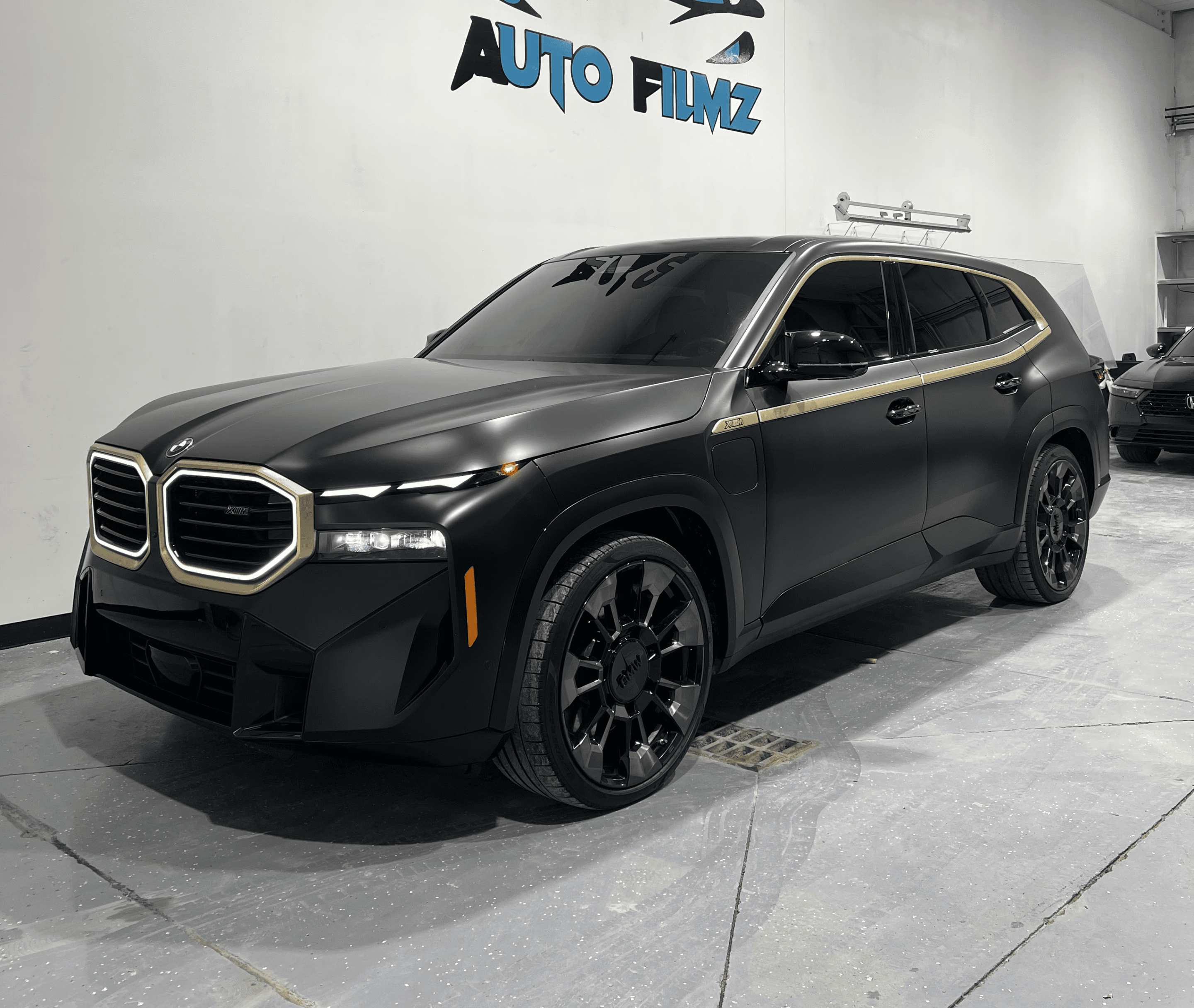 A matte black BMW XM luxury SUV is parked indoors on a polished concrete floor.