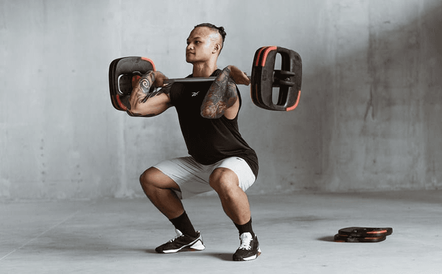 Ein Mann führt eine Kniebeuge mit Langhantel während eines Bodypump-Kurses aus.