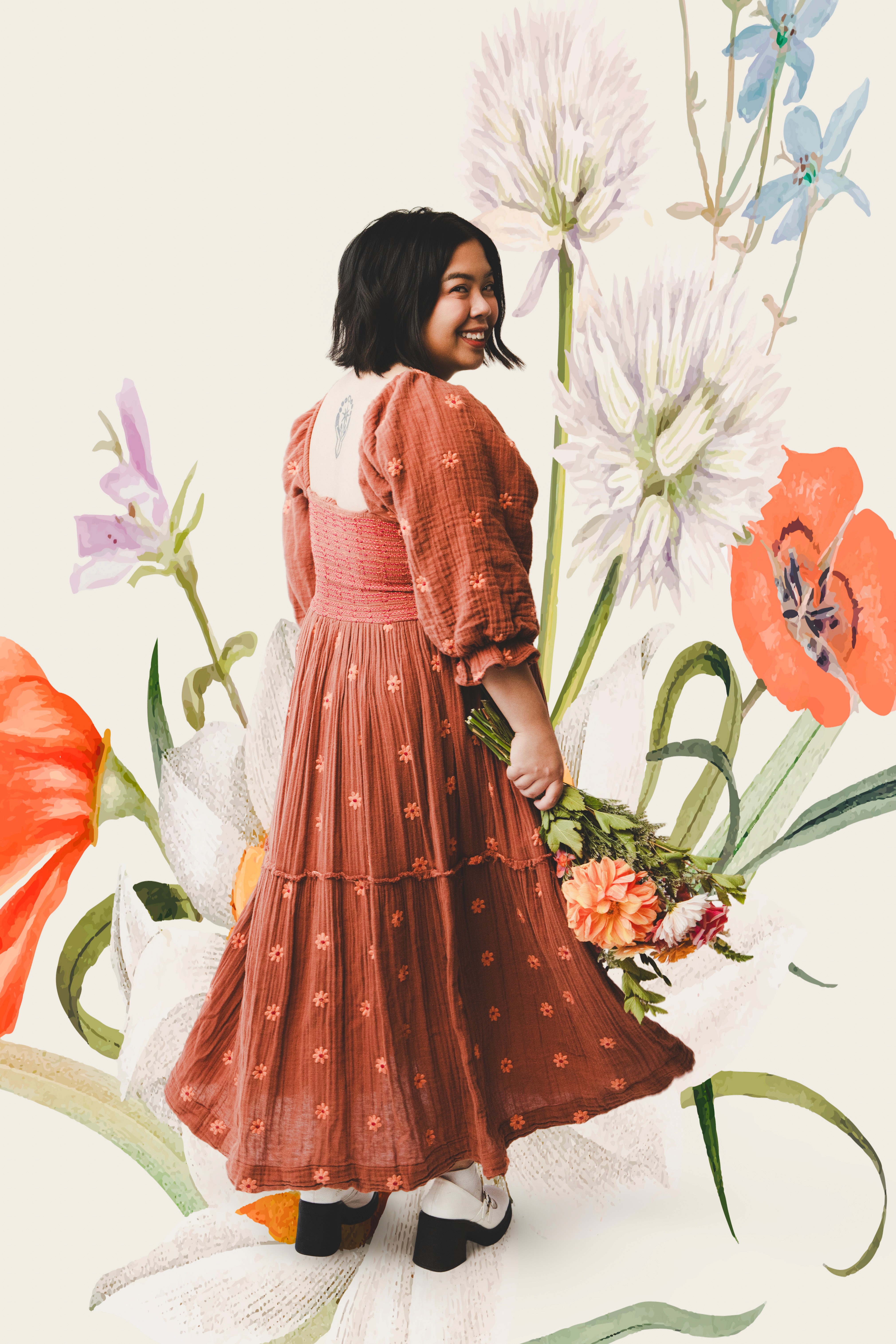 Kelly, the designer, in rust coloured dress holding flowers against a floral backdrop