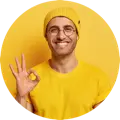Smiling person wearing a yellow shirt and beanie, making an "OK" gesture against a yellow background.