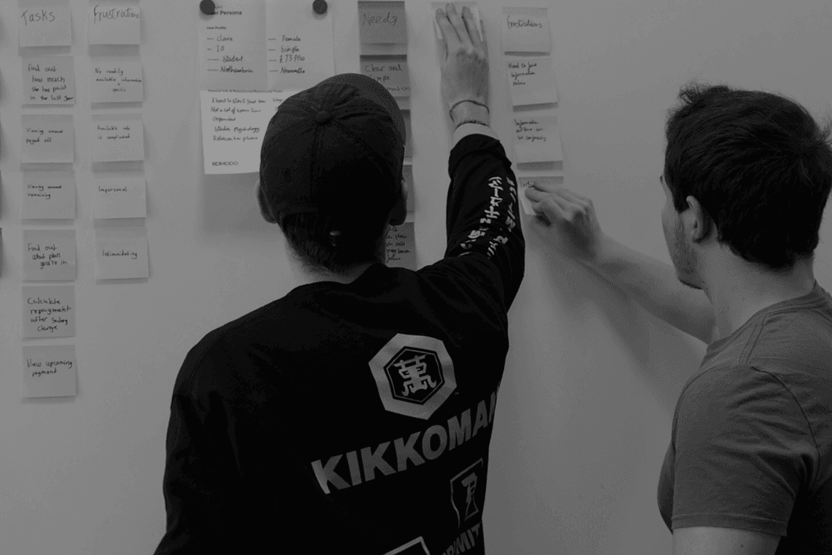 Two people putting post it notes onto a whiteboard
