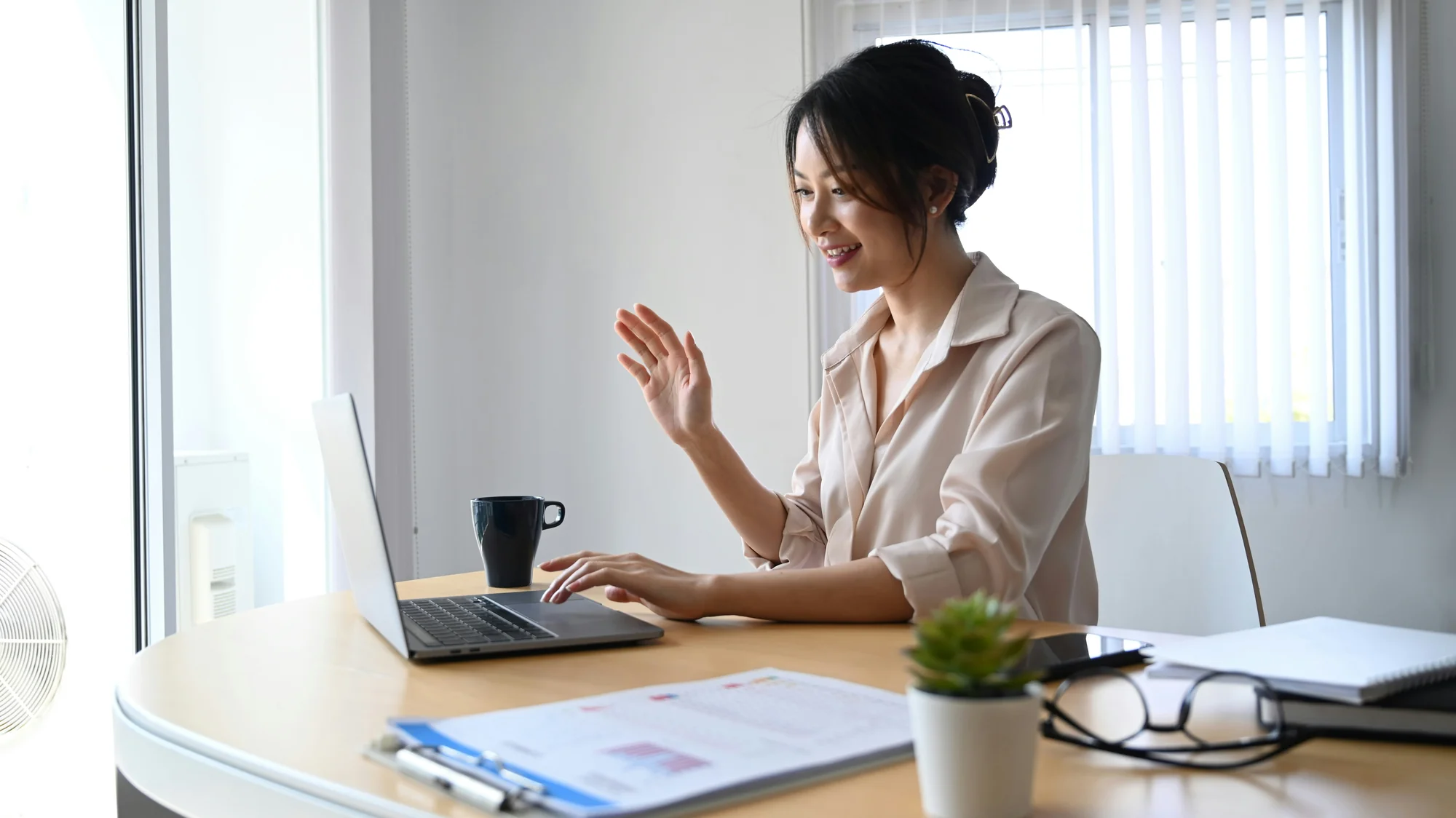 Professional waving during video call at desk with laptop