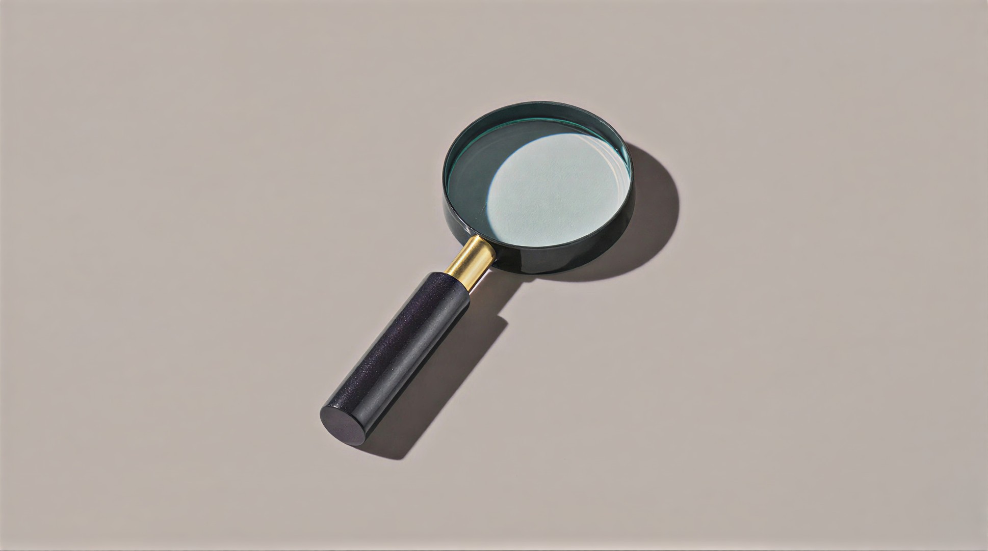 A black-handled magnifying glass with a gold neck is angled slightly to the right against a light beige background, casting a soft shadow.