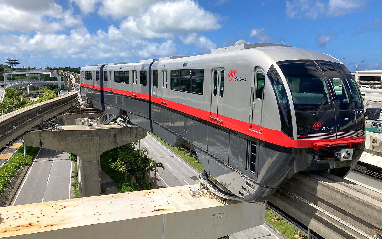 Το τρένο του Μονορέιλ της Οκινάουα ταξιδεύει στις υπερυψωμένες ράγες κάτω από έναν γαλάζιο ουρανό.