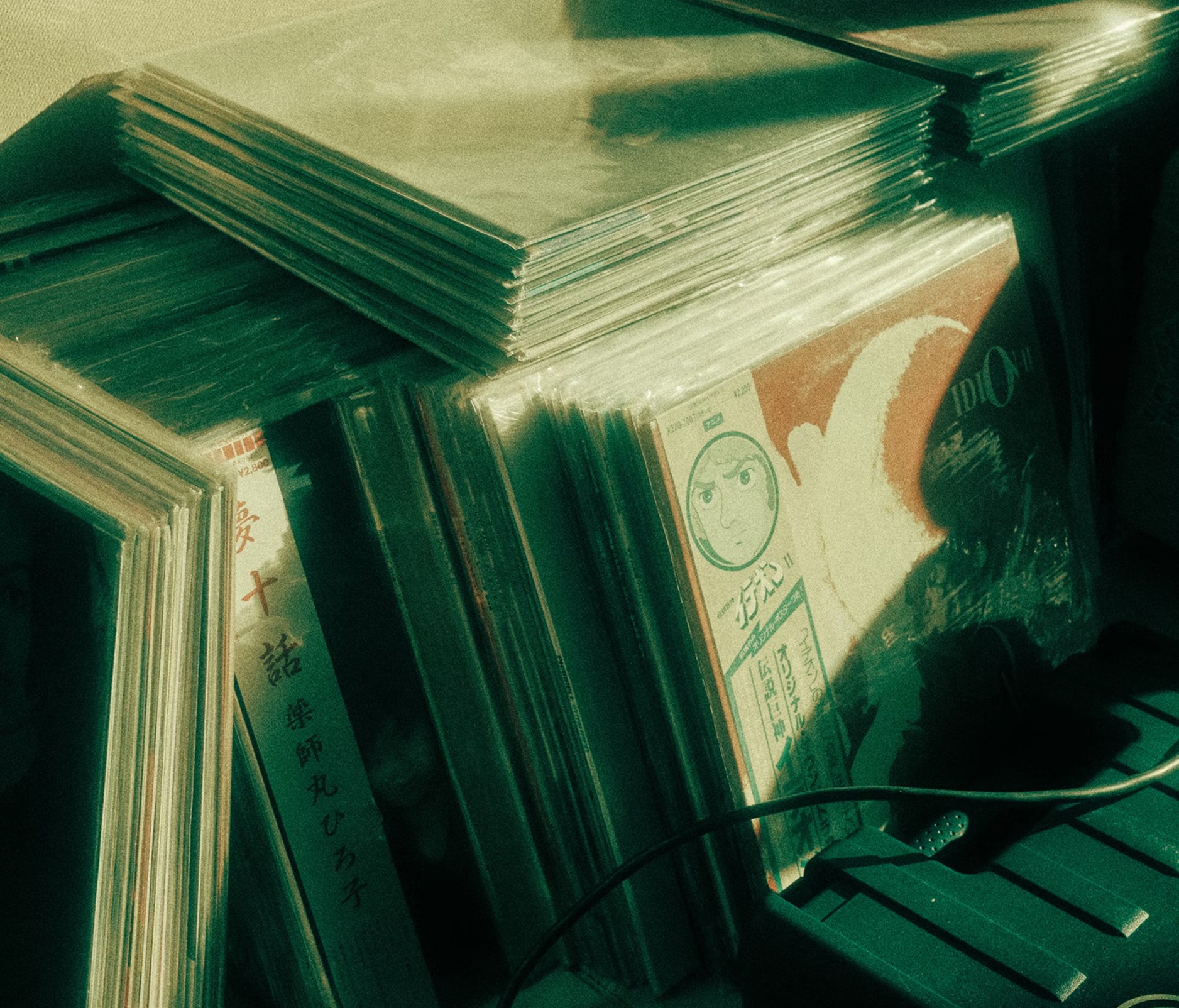 Stack of vinyl records leaning in a crate, illuminated by green-tinted light.