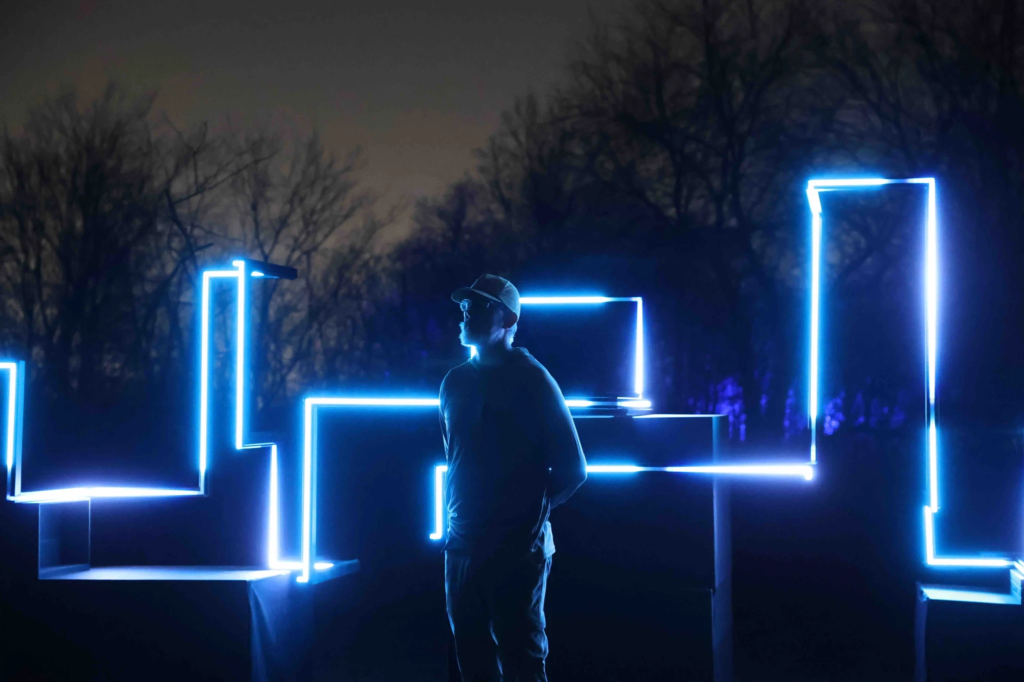 A person stands among glowing blue rectangular structures at night, surrounded by a dark landscape.