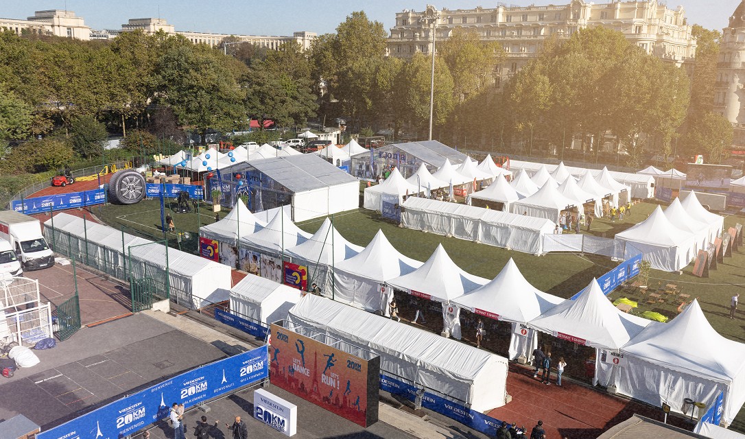 Vue aérienne d'un événement extérieur à Paris avec plusieurs tentes blanches, stands, panneaux et des participants en arrière-plan.