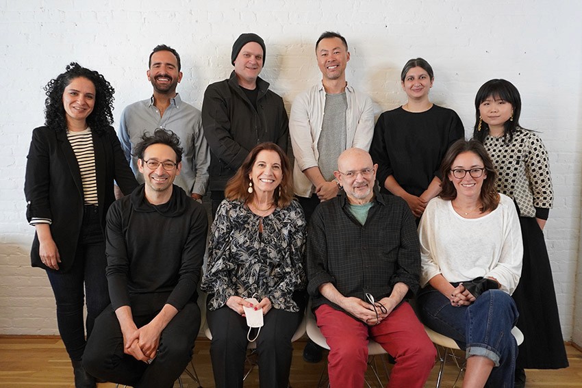 Group portrait with ten people, six standing in the back row and four sitting on chairs in the front row, and they all have smiles on their faces