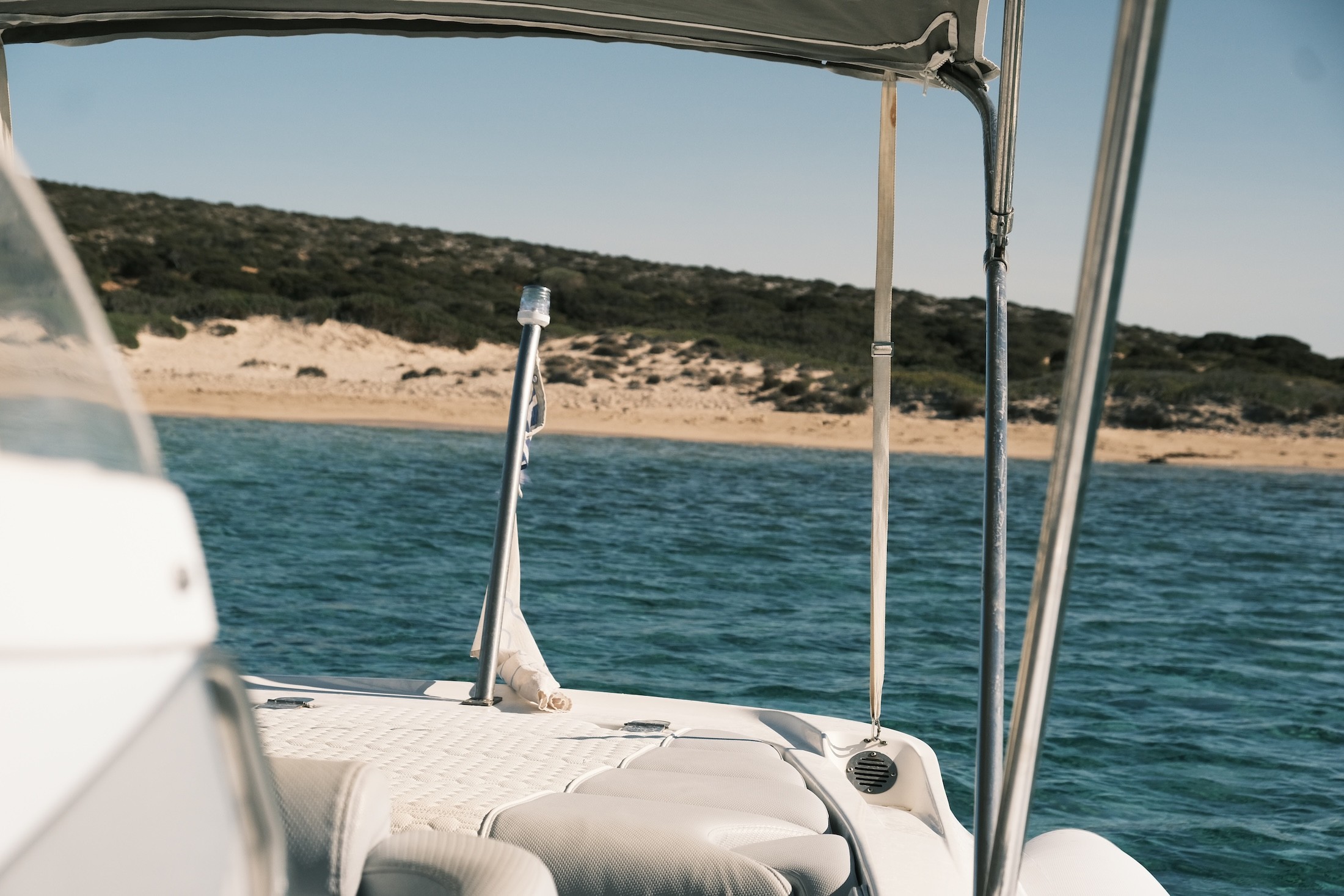 White motor yacht anchored in turquoise waters near a rocky coastline with a traditional Greek chapel and distant Cycladic islands.