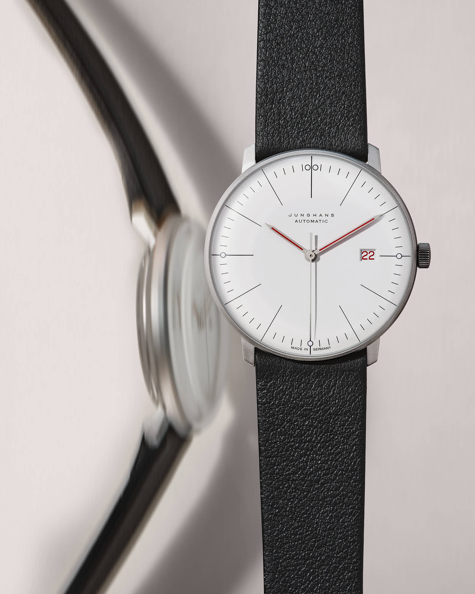 Minimalist watch with black leather strap, white dial, and red accents.