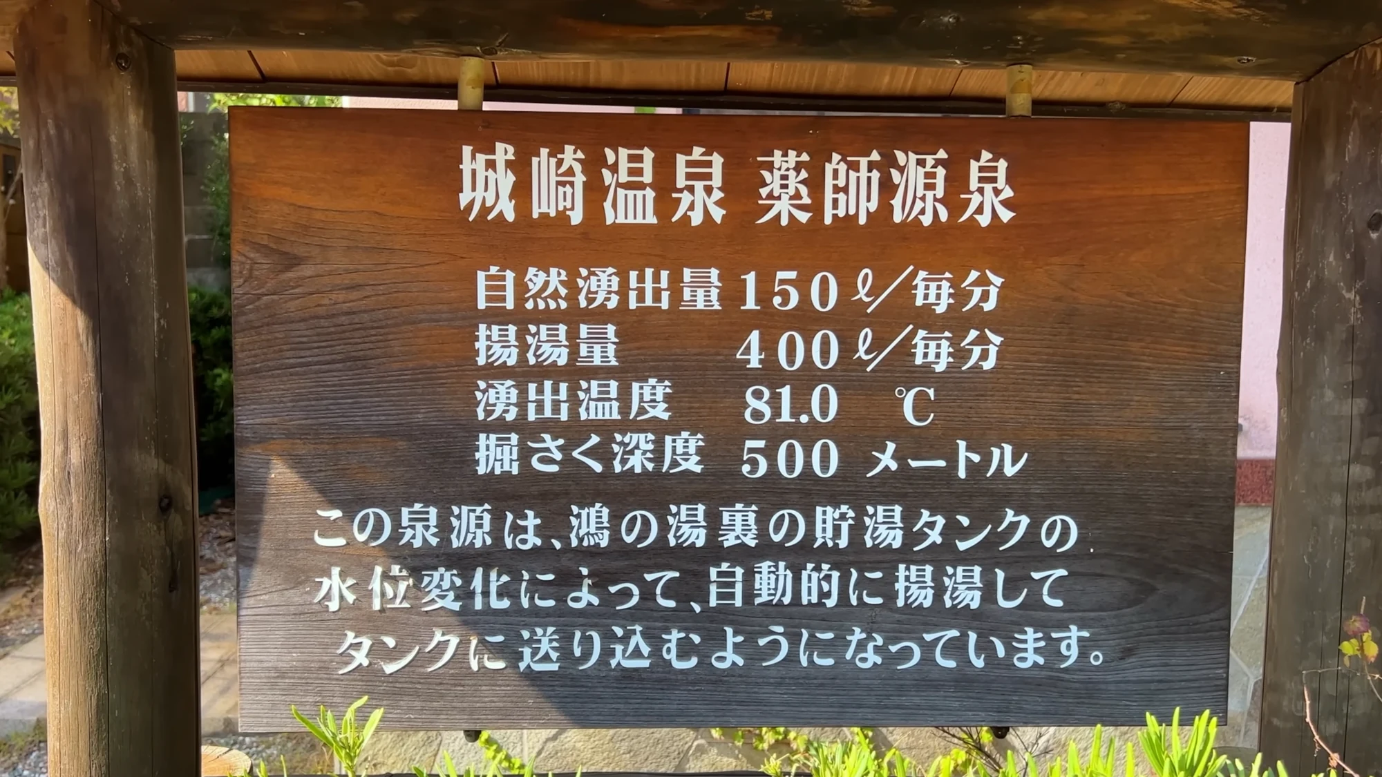 Wooden signboard at Kinosaki's Yakushi source spring listing flow rate, temperature and bore depth in Japanese.