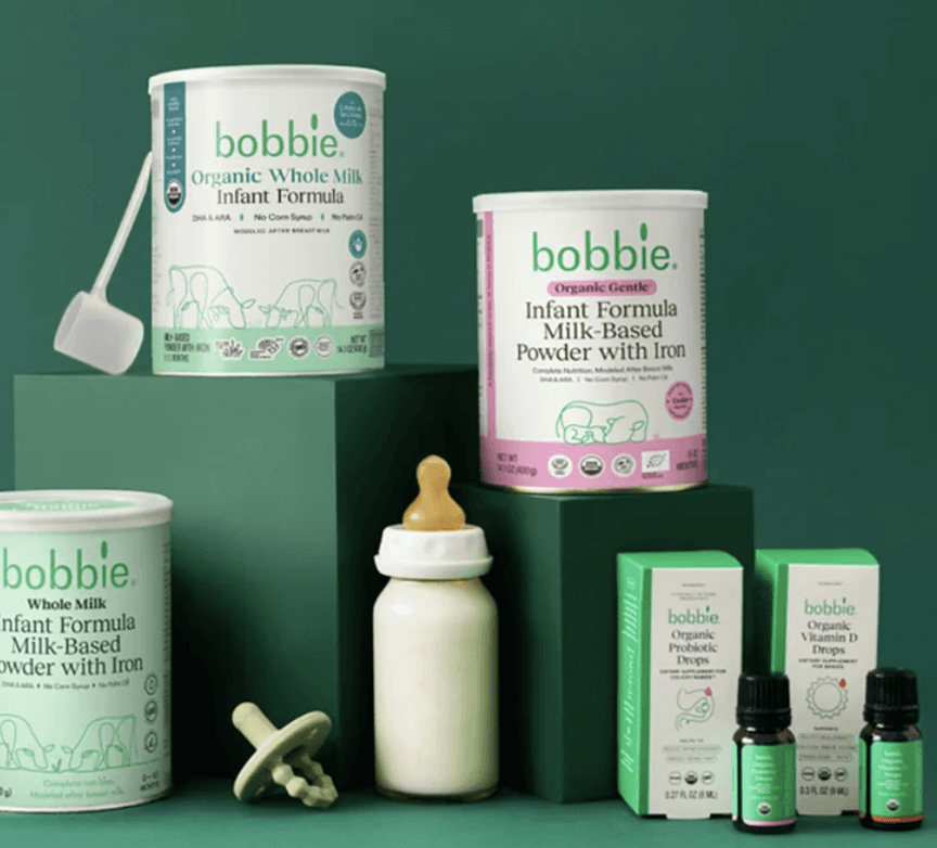 A hand pouring cherry vanilla flavoured soda from a colorful can in a tall glass, over a soft sky blue background, with two more cans on the side. Grape and Root Beer flavoured.