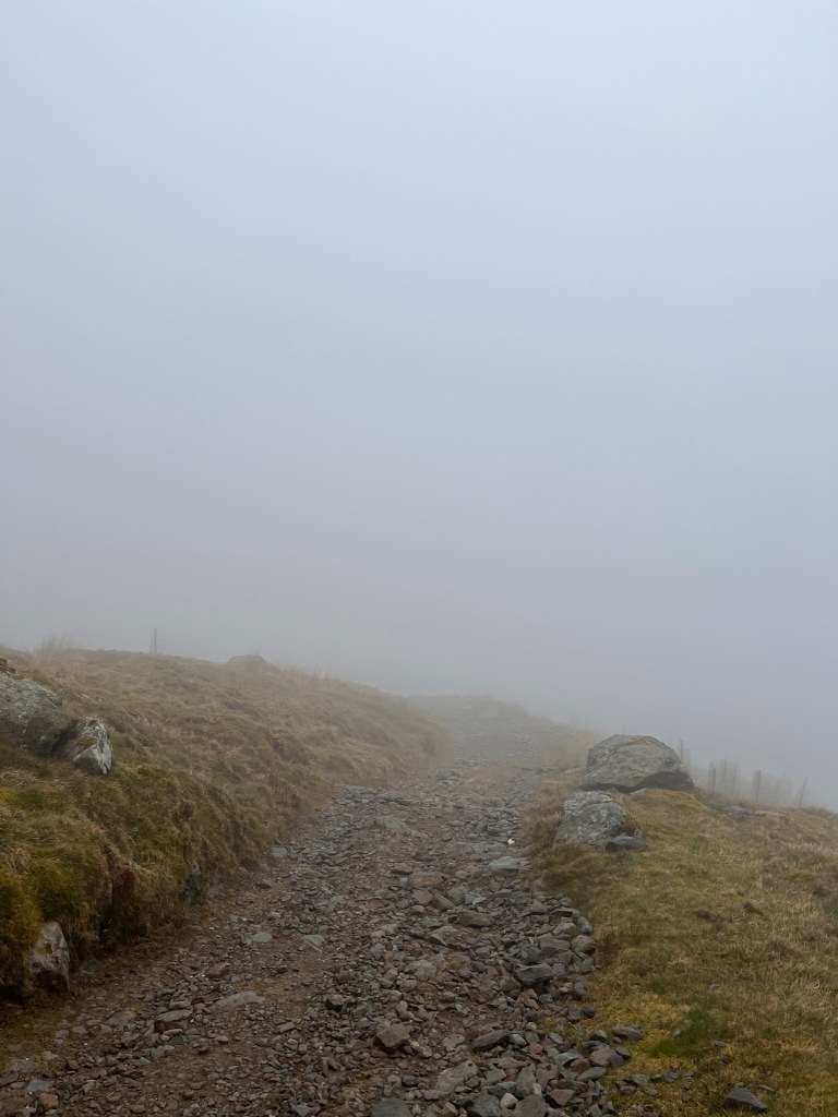 Intense fog hides 3/4 of the image. A stony path leads into the fog.