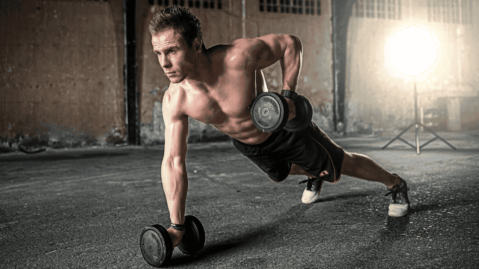 Gemini said A shirtless man performing a renegade row with dumbbells in a rustic gym setting.