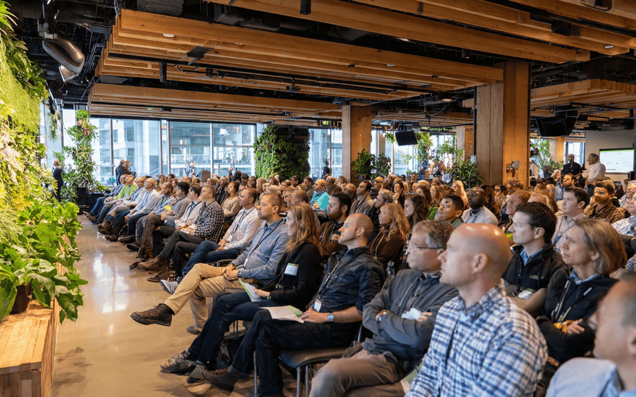 A large audience seated in a modern lecture hall with wooden beams and vertical gardens on the walls.A large audience seated in a modern lecture hall with wooden beams and vertical gardens on the walls.