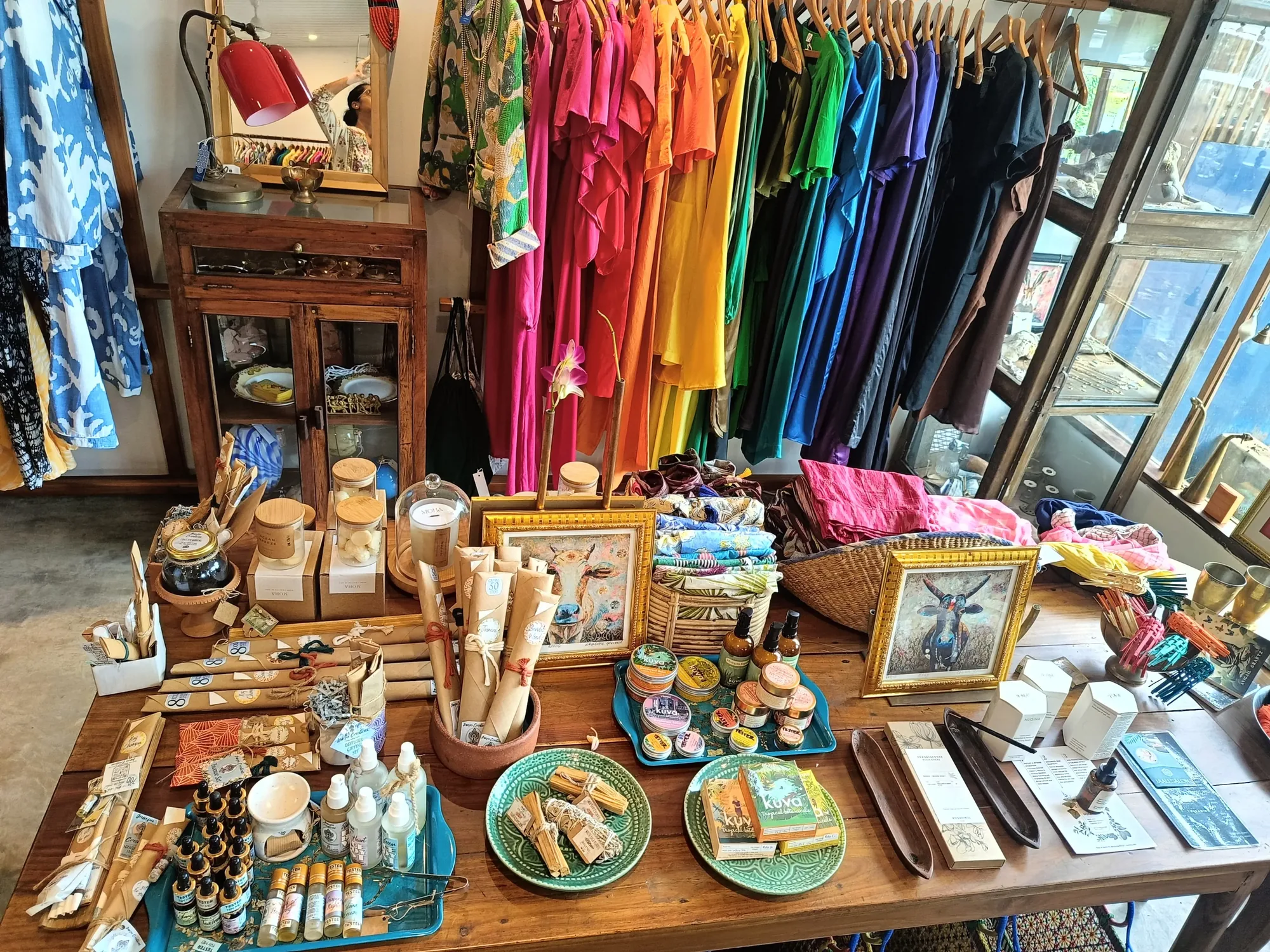 Gift table of candles, incense and oils backed by a rainbow rail of linen dresses at Jaali Boutique