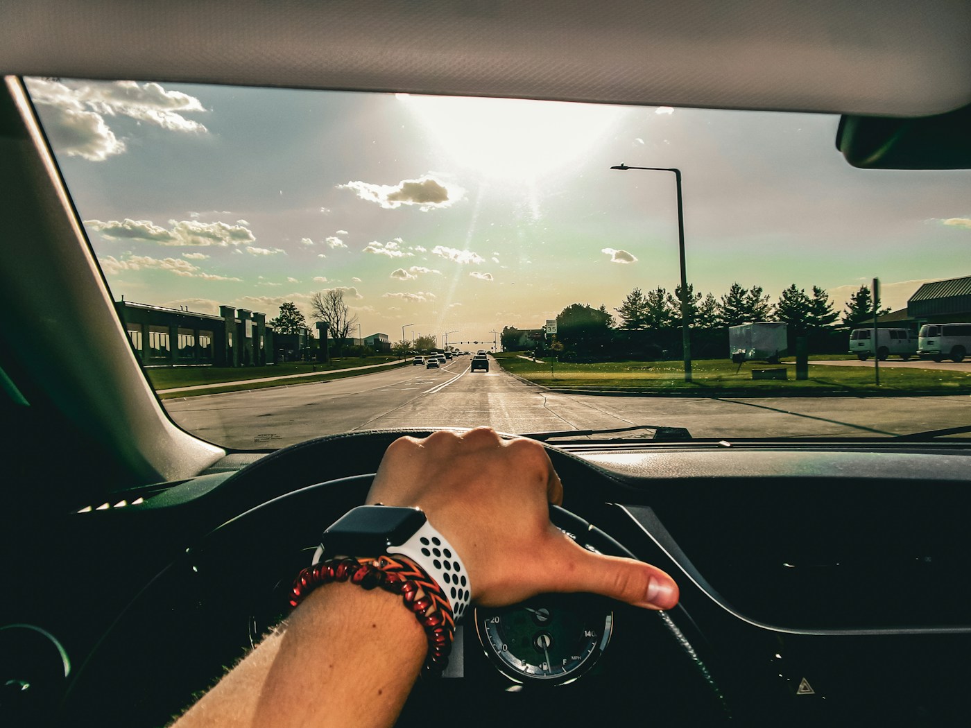 A driver's hand on the steering wheel, with a straight road ahead through the windscreen