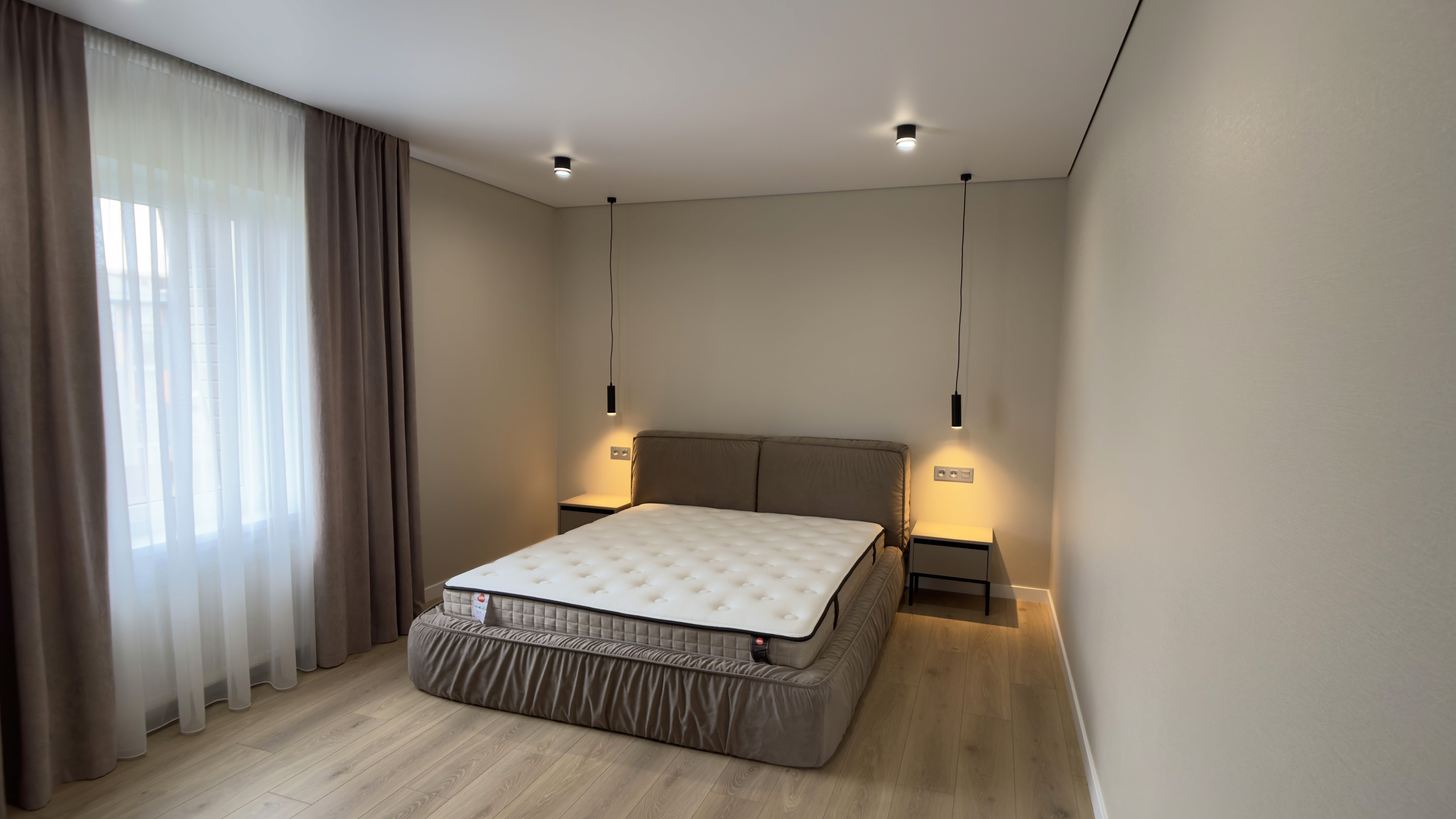 Світла спальня з великим ліжком, підвісними світильниками та щільними шторами