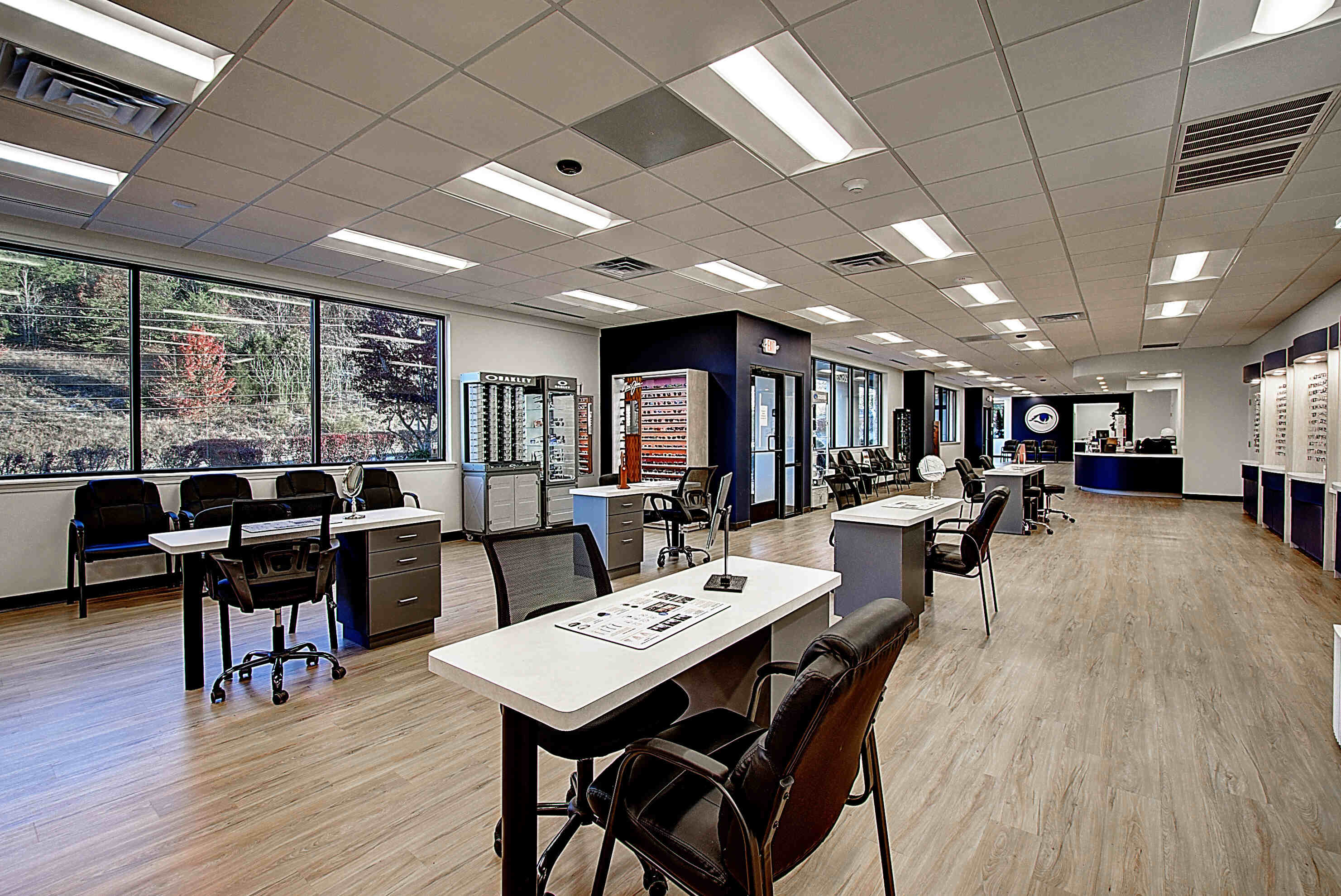 An open retail space with multiple desks, chairs, and large windows, featuring modern decor and bright lighting.