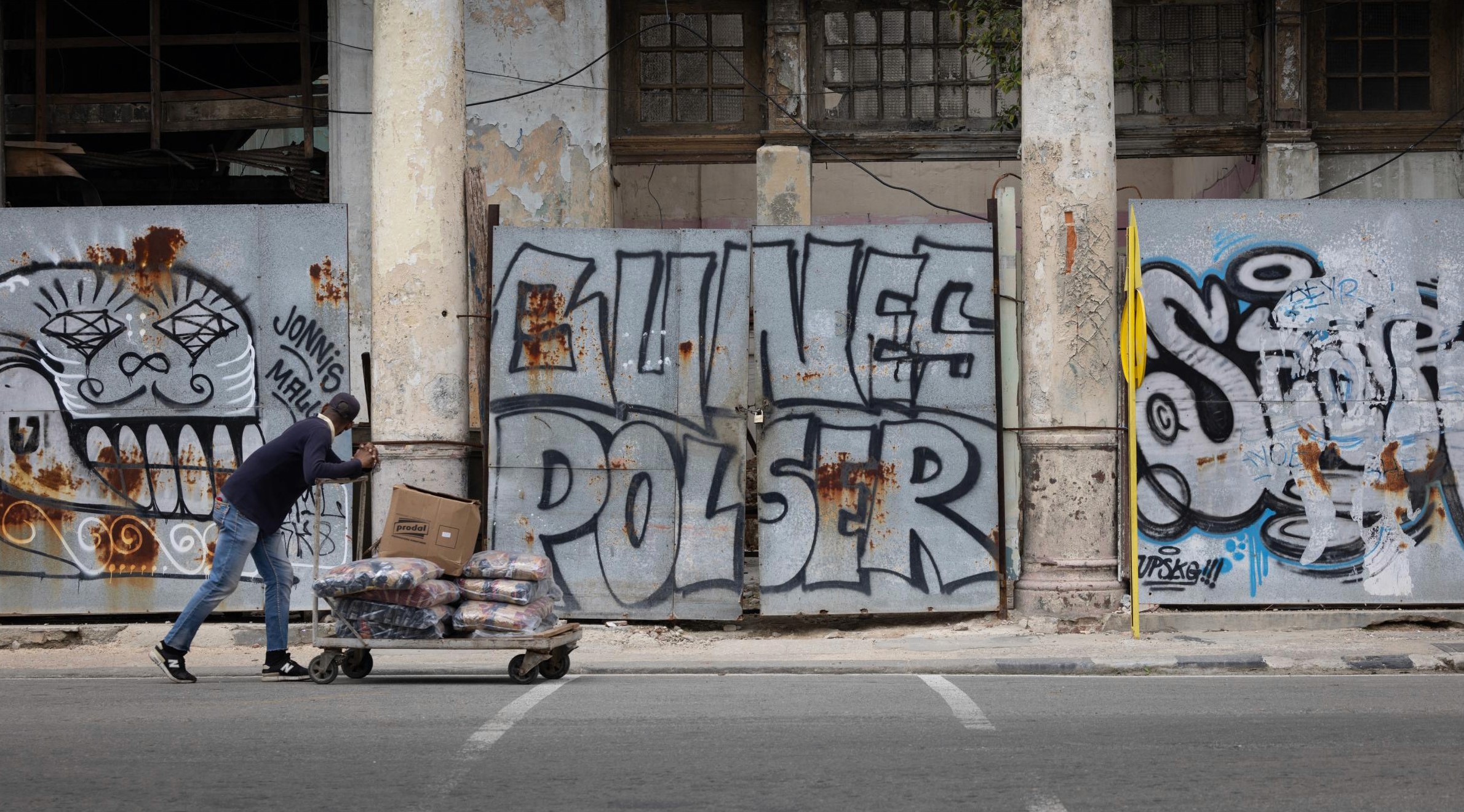 Worker pushes a cart near a wall of graffiti - Havana, Cuba