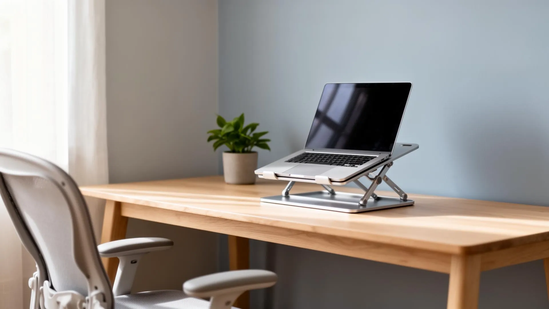 Minimal home office workspace with a laptop on an adjustable stand, wooden desk, ergonomic chair, and natural light