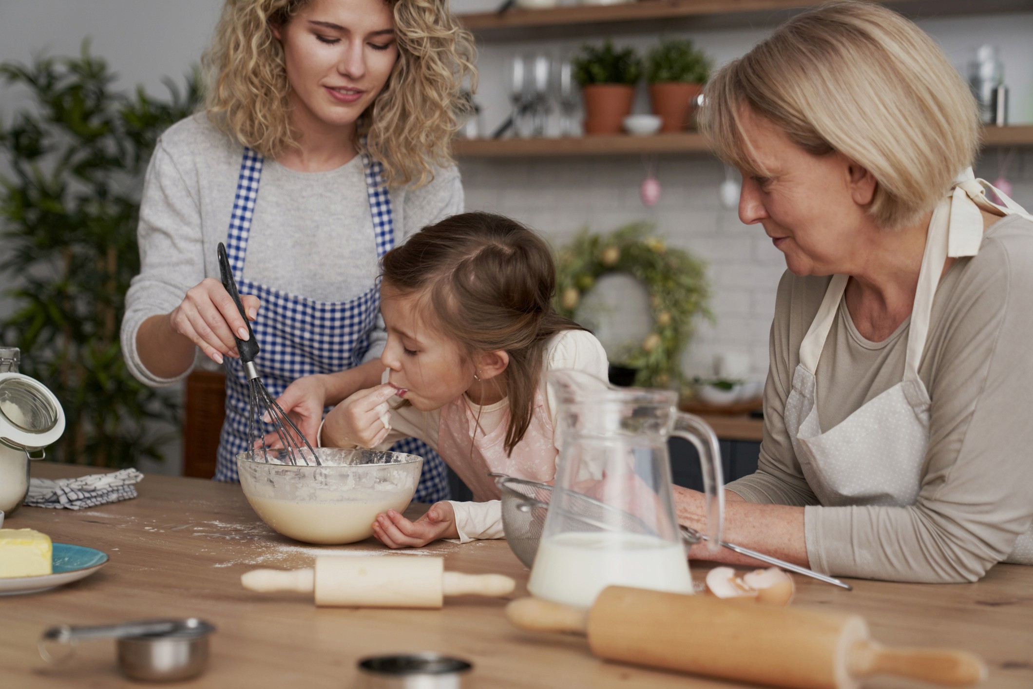 Abuela cocinando con su nieta y una mujer joven en la cocina, compartiendo un momento familiar gracias al uso de ayudas auditivas