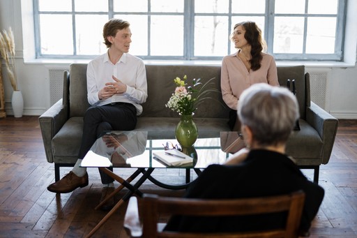 A photo of a couple sitting on couch with another person on chair across from them