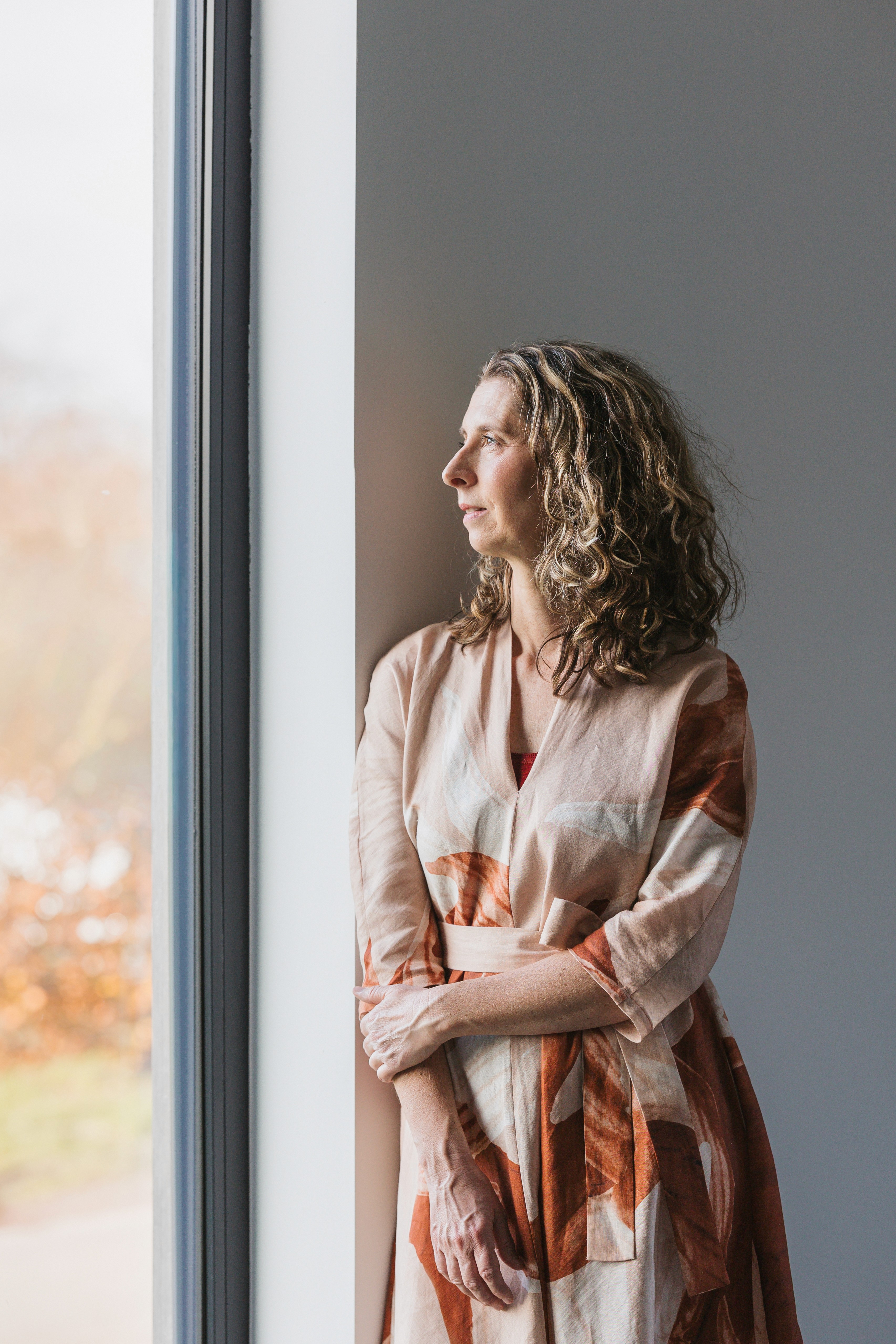 Tanja van Elburg staat bij het raam en kijkt rustig naar buiten.