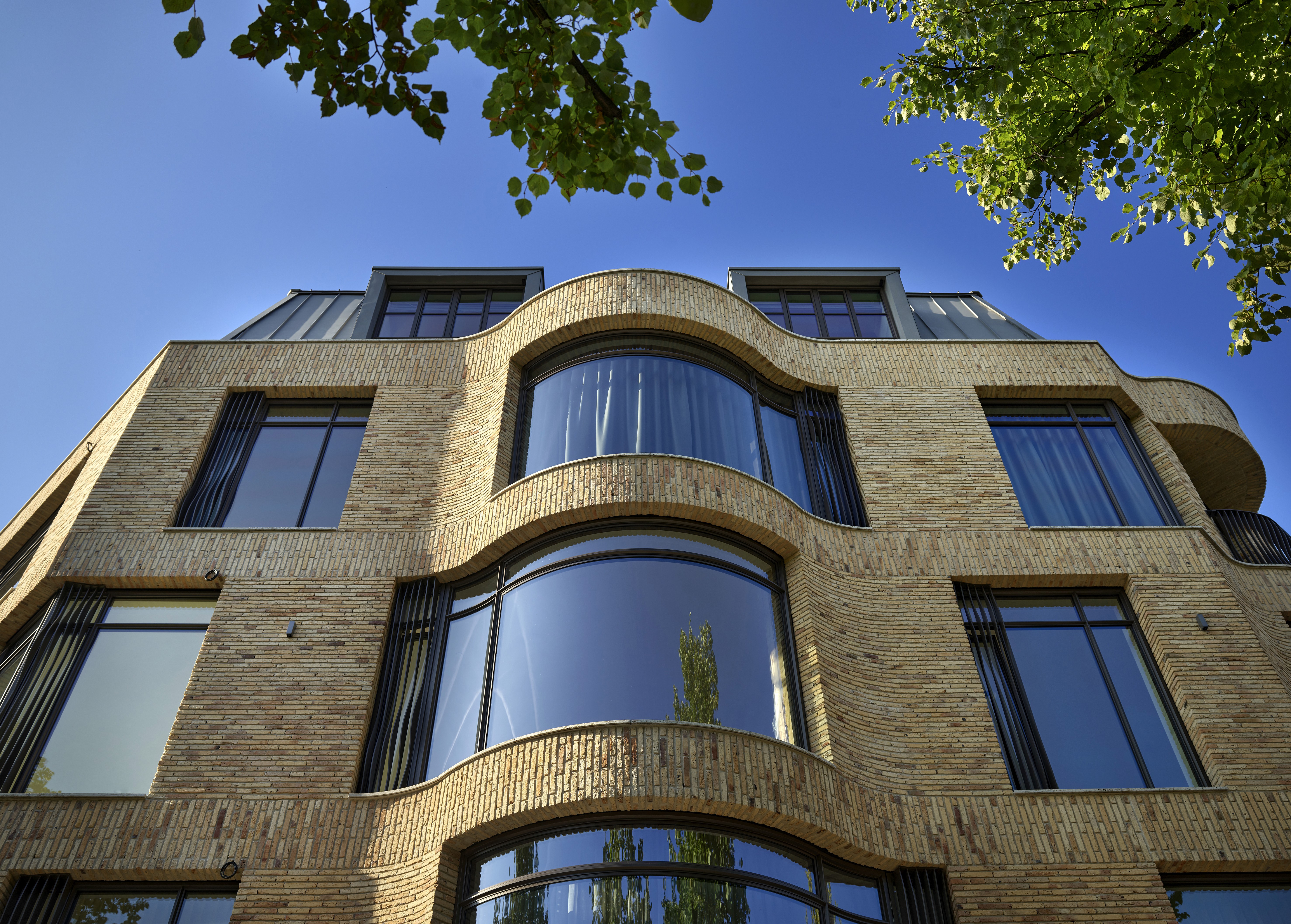 Gebouw met gebogen gevel en grote ramen, gezien van beneden met bomen erboven.