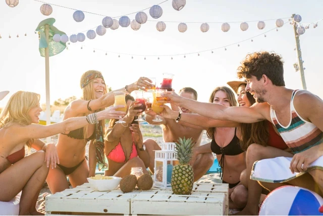 A group of friends having a beach party during the day and drinking together.