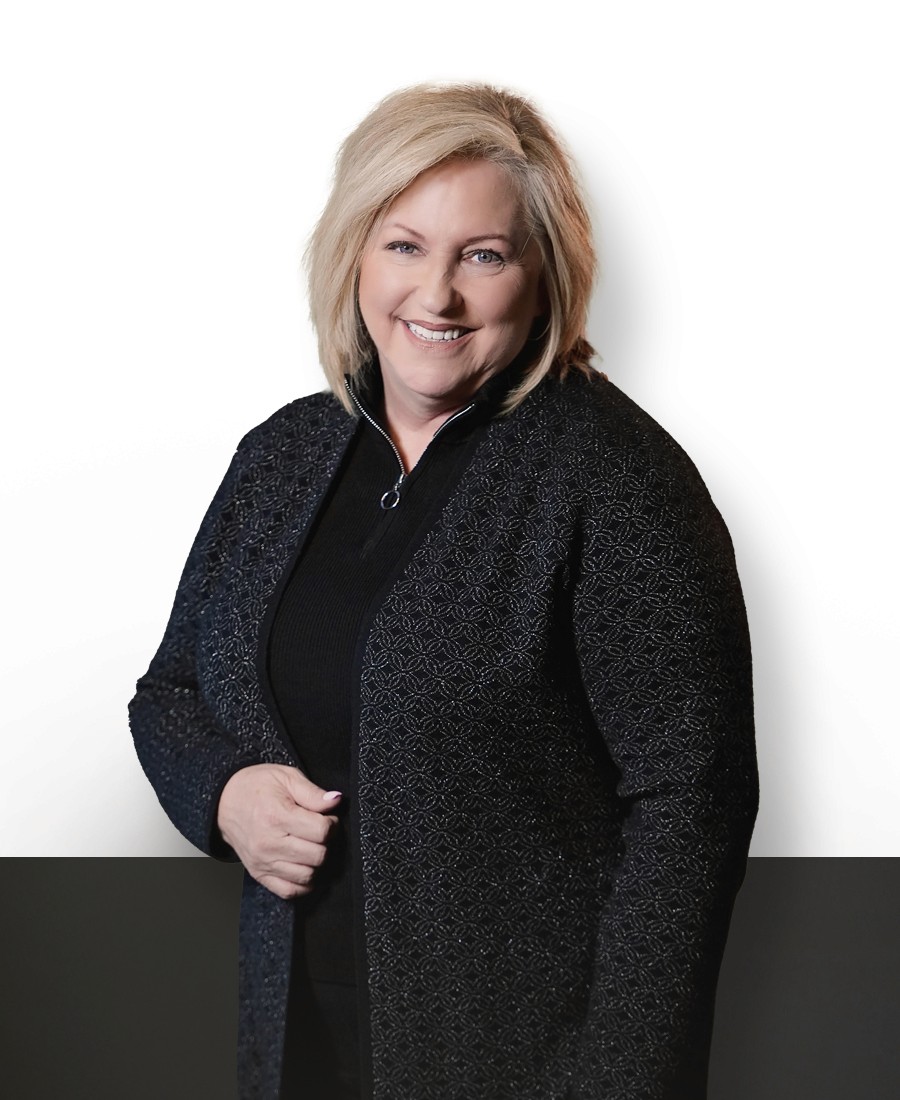 corporate headshot of female with light skin and blonde shoulder-length hair smilng warmly. Wearing a dark grey coat and black zippered pullover. 