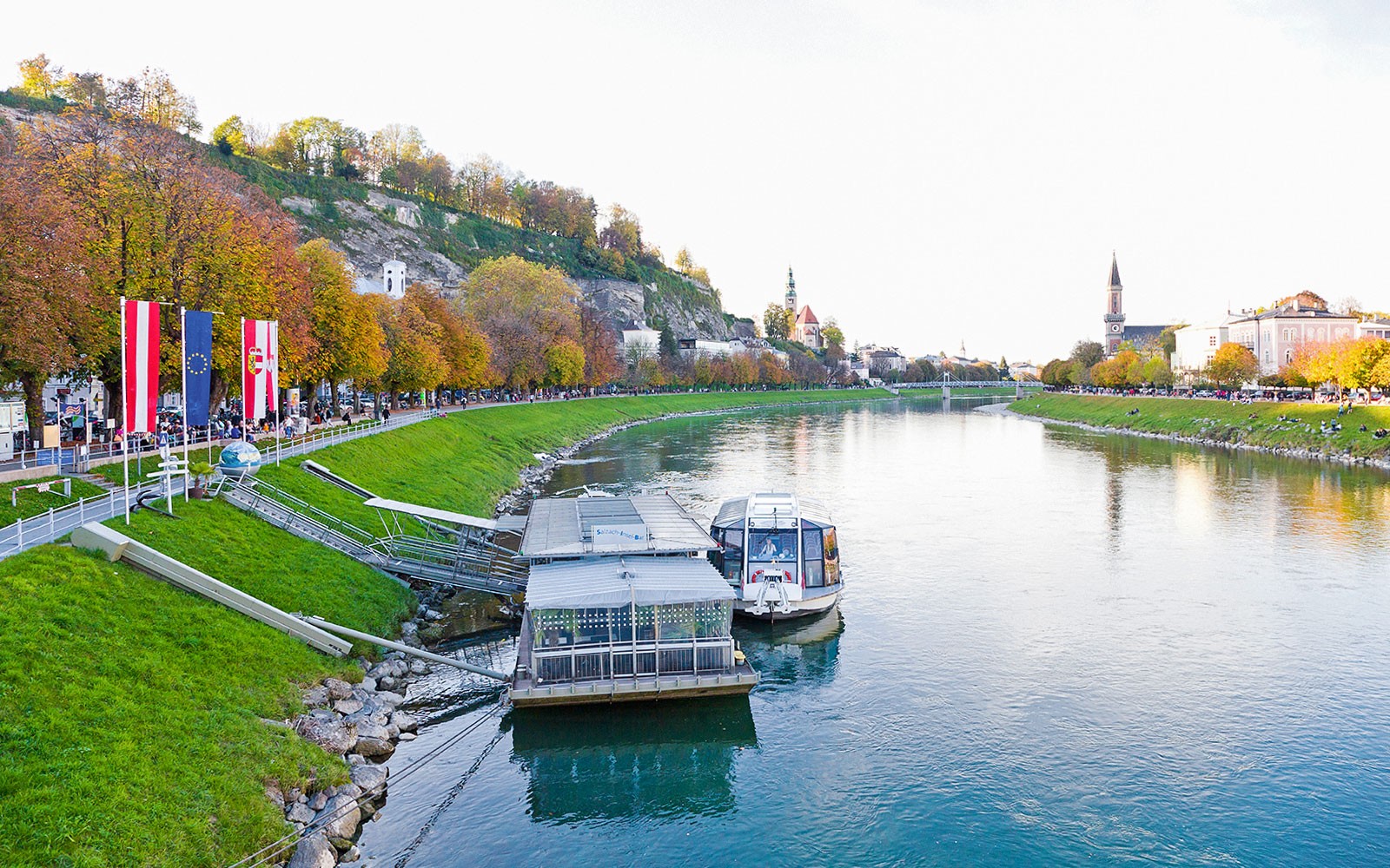 萨尔茨堡,奥地利,萨尔扎赫河上的游船码头,周围是秋天的树木和城市景观。