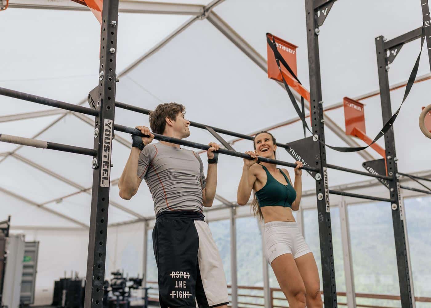 Man and woman performing pull-ups in an empty gym.