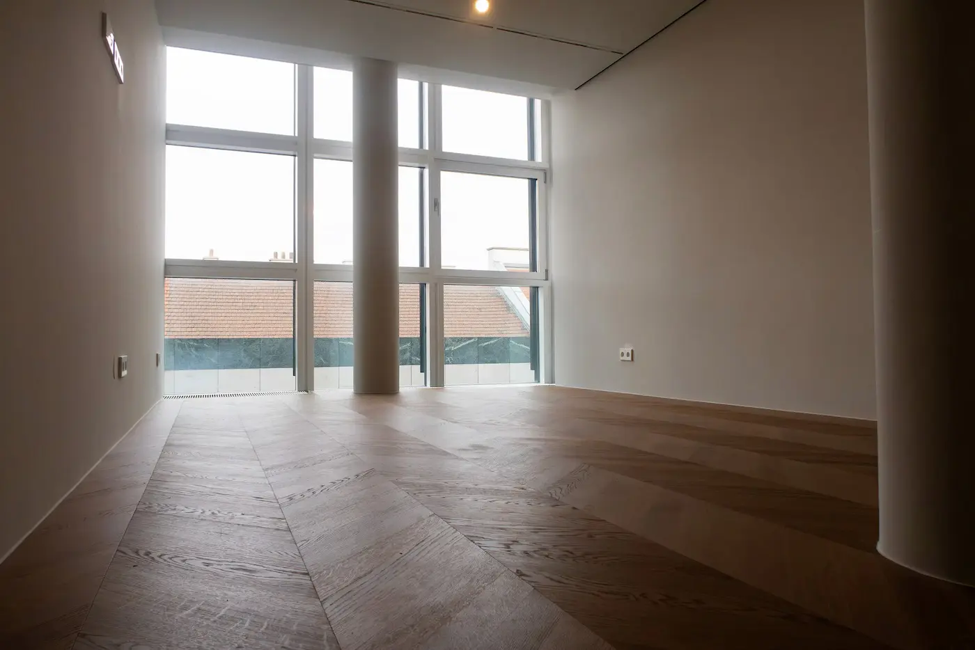 Heller Wohnraum mit großer Fensterfront und frisch verlegtem Chevron-Parkettboden.