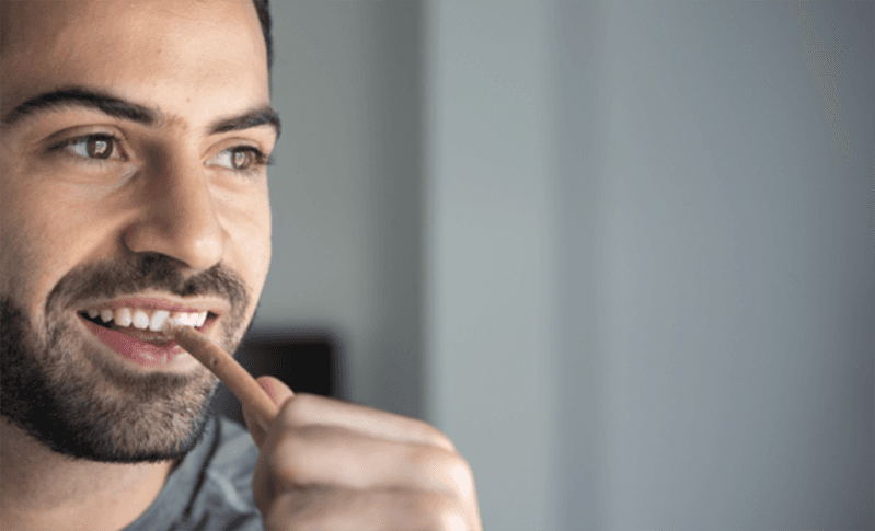 A man holding an ecological toothbrush that looks like a stick with threads,