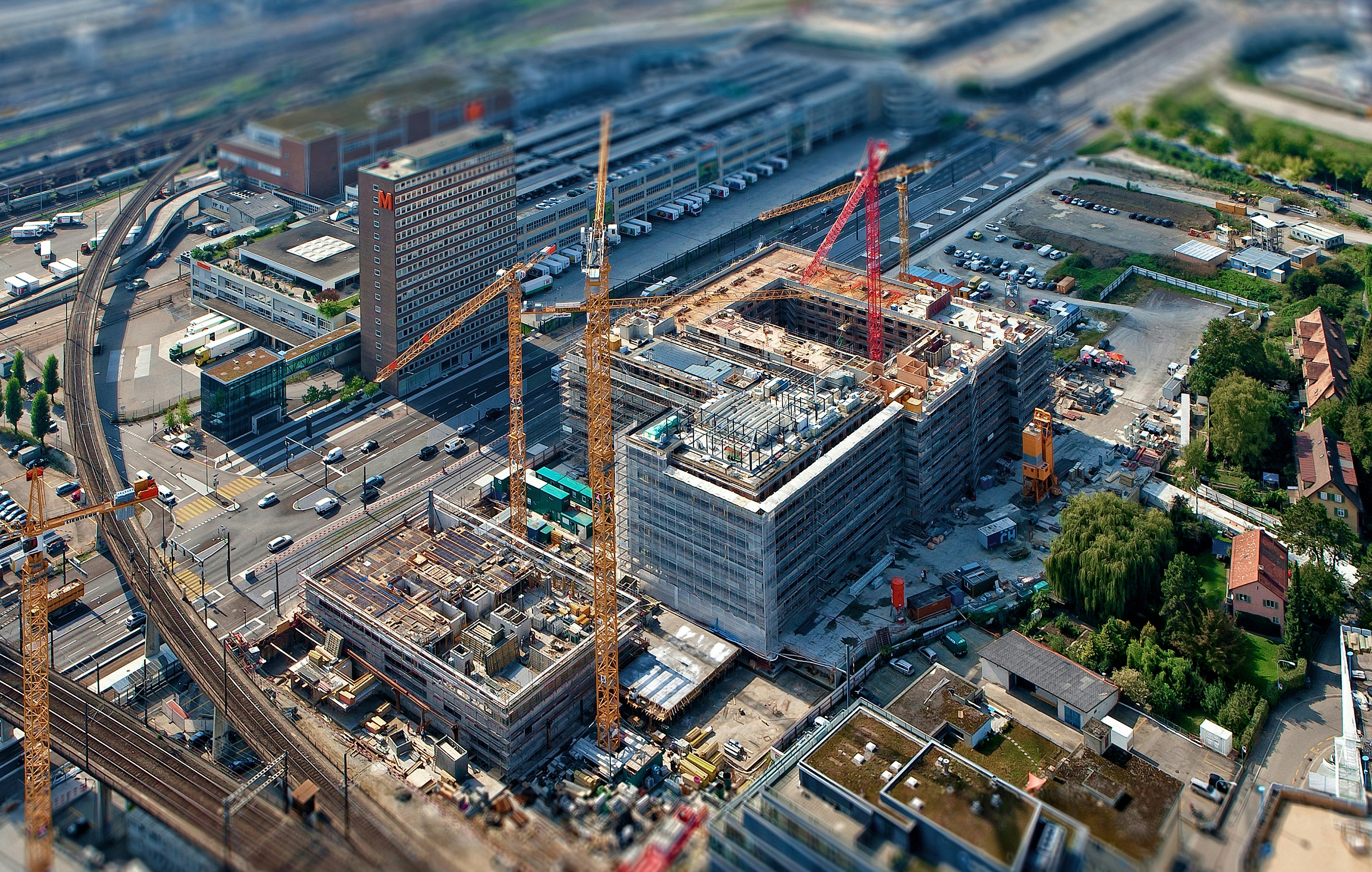 Aerial view of an active urban construction site with red cranes and multi-story buildings under development